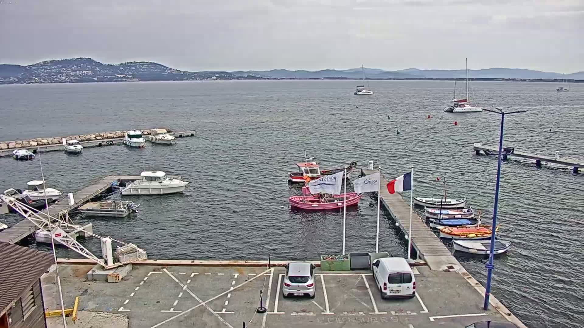 A harbor filled with various boats under a cloudy sky, with mountains visible in the distance.