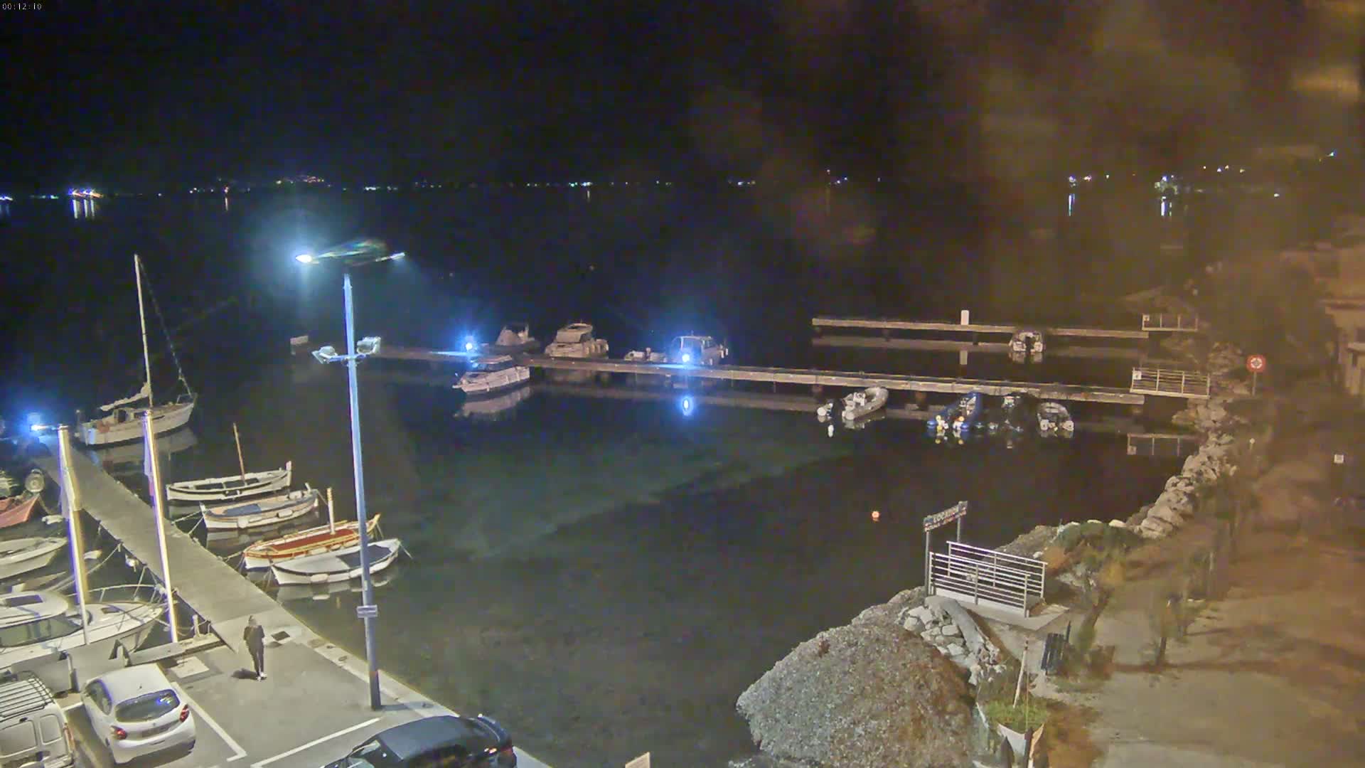 A nighttime view of a harbor with numerous boats docked at piers, under calm, dark conditions.