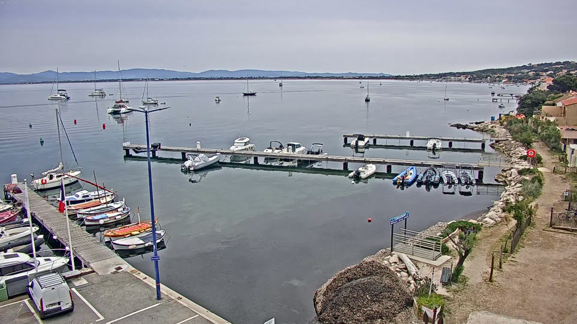 A calm bay with numerous boats docked at piers and moored in the water, under an overcast sky.
