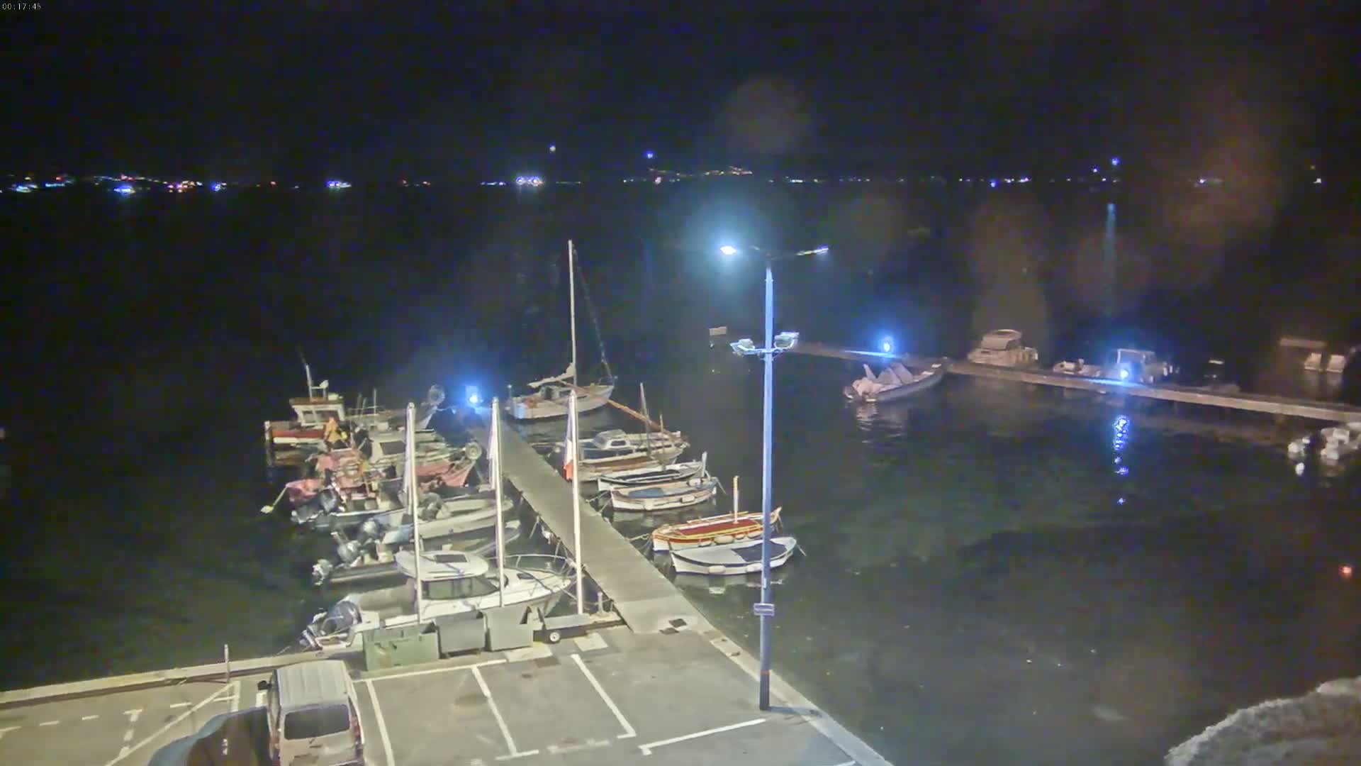 A nighttime view of a harbor with numerous boats docked along a pier, under a clear, dark sky.