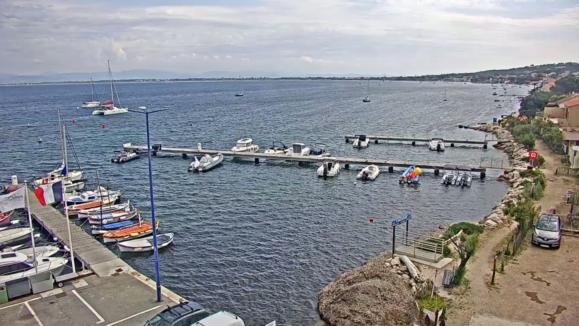 A marina with numerous sailboats and motorboats docked at piers under a partly cloudy sky.