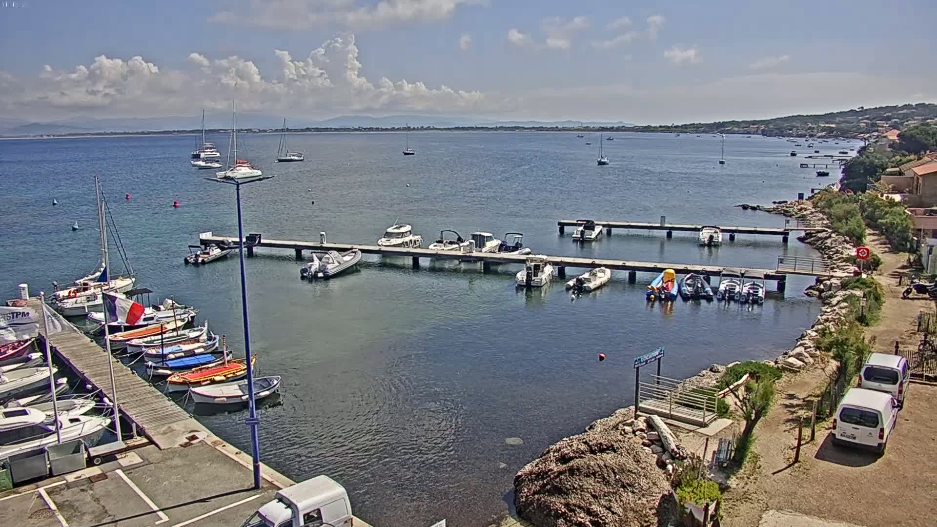 Numerous boats are moored at docks along a calm body of water under a partly cloudy sky.