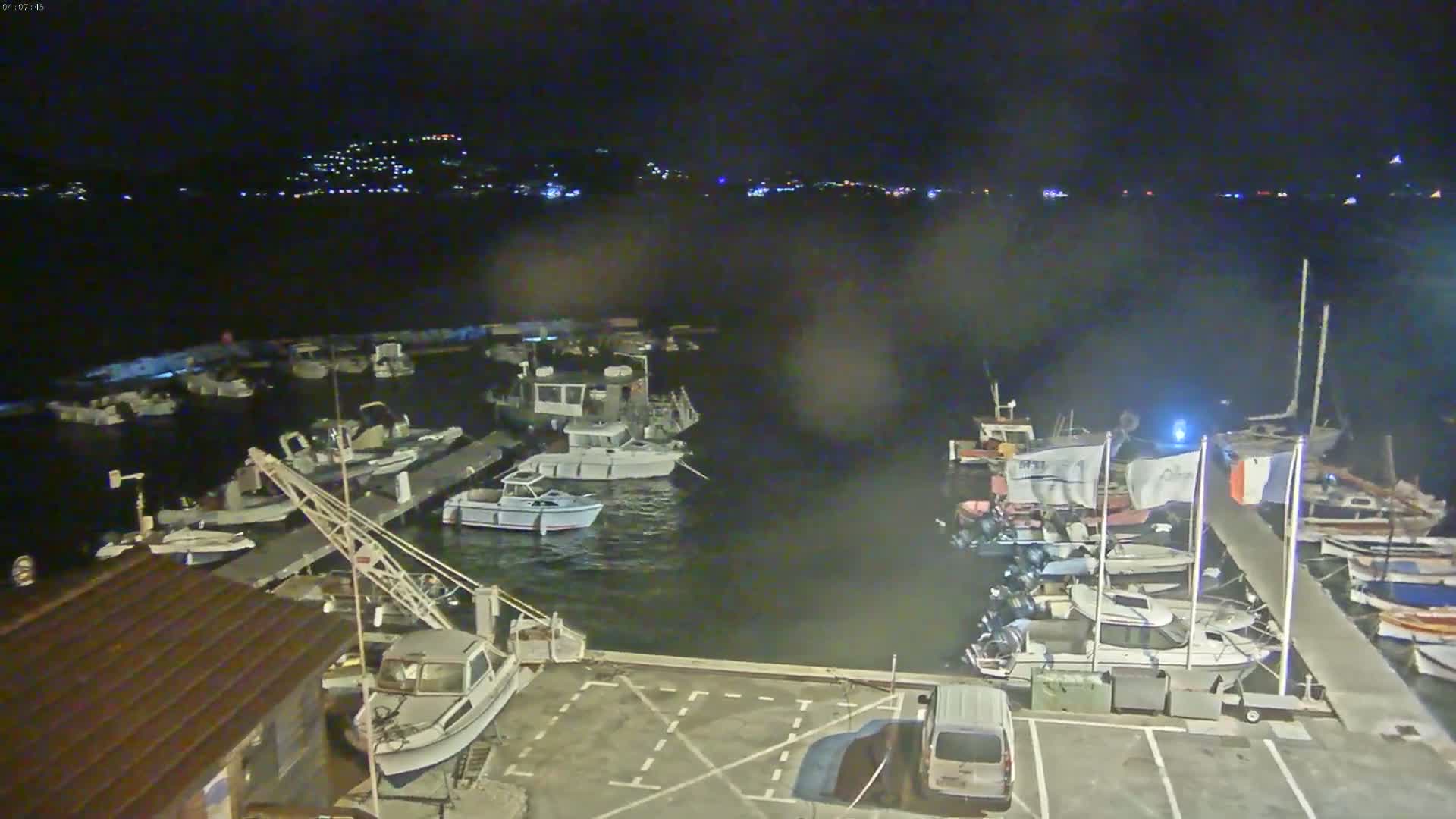 A nighttime aerial view shows a marina filled with numerous boats moored at docks under a dark sky.