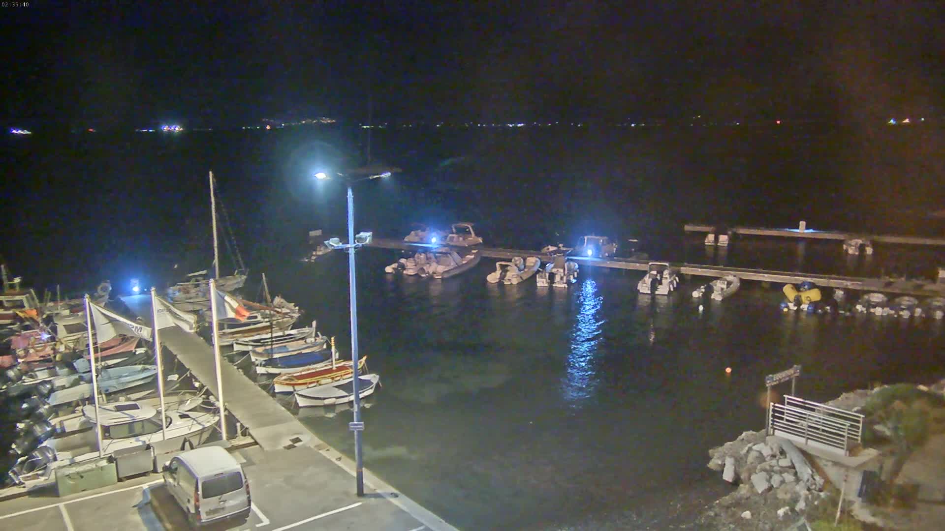 A nighttime view of a marina with numerous boats docked, some illuminated, under a clear, dark sky.