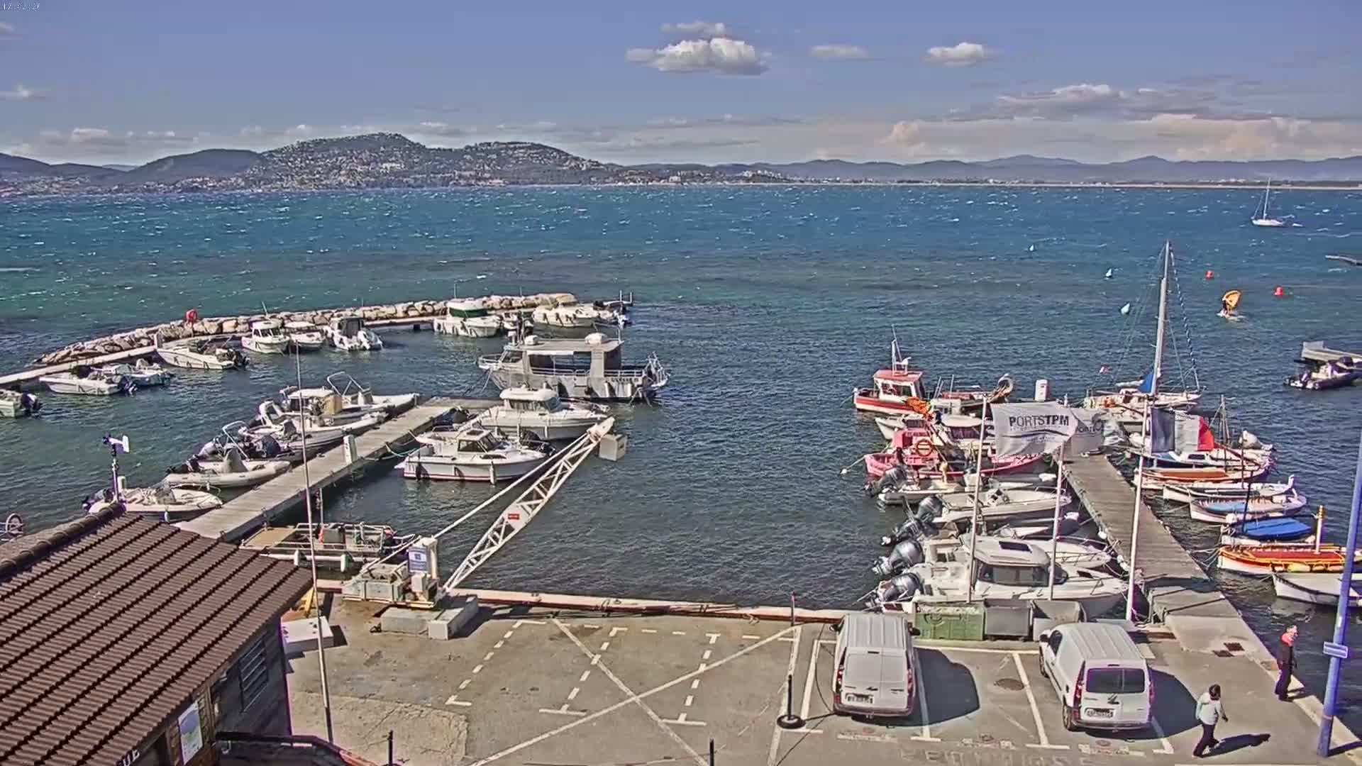 A marina filled with numerous boats and yachts is shown under a partly cloudy sky with a windy sea.