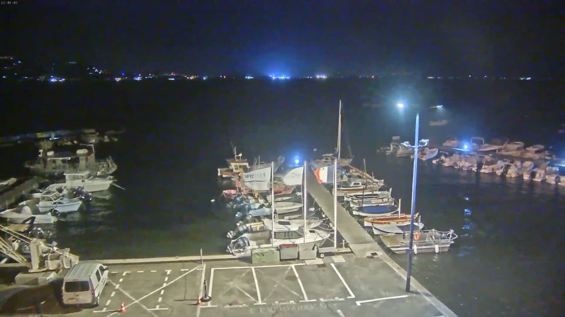 At night, numerous boats are docked at a marina, with a van parked in an empty lot nearby.