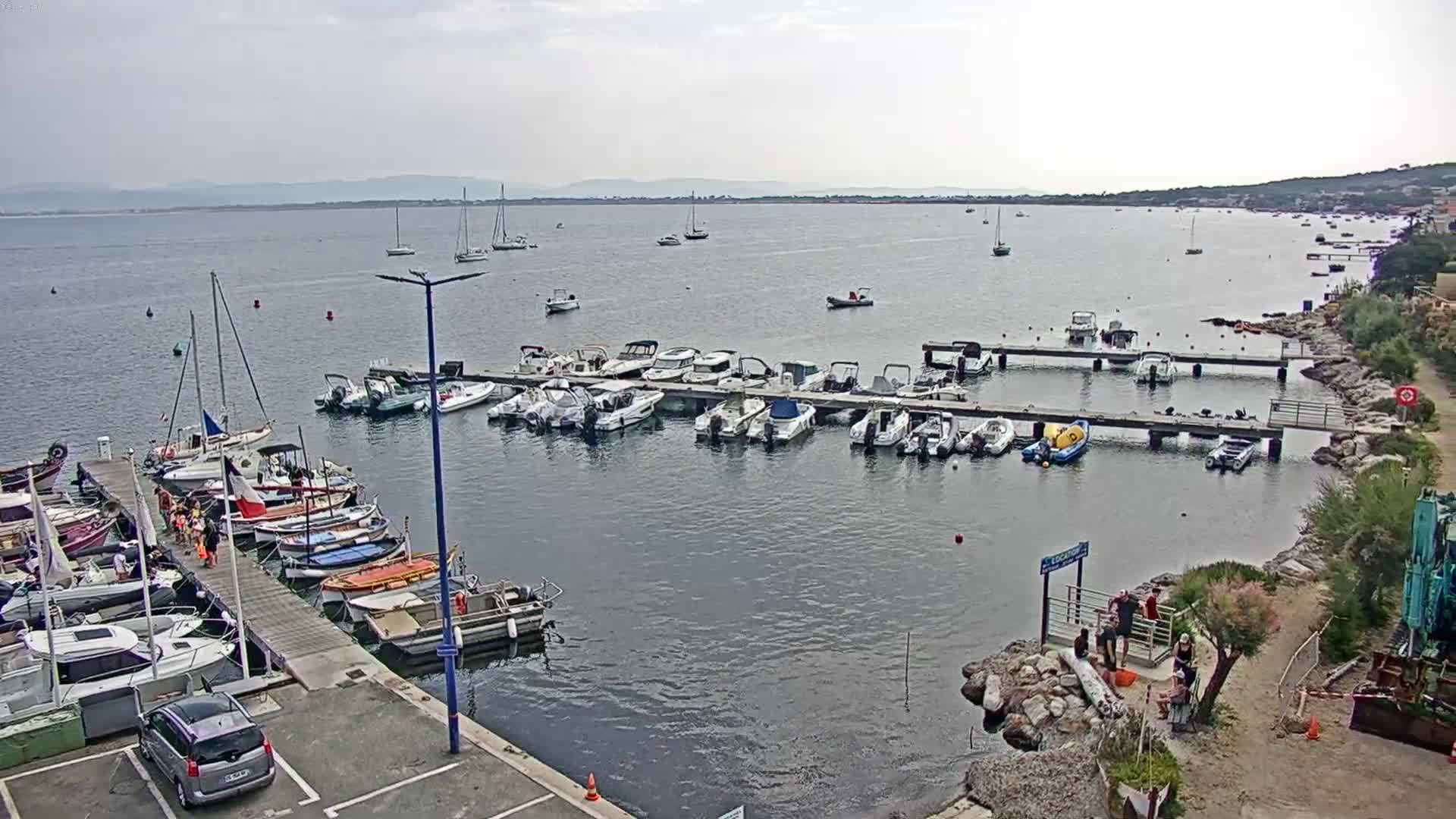 A marina filled with numerous boats and sailboats is situated on calm, overcast water next to a rocky shoreline.