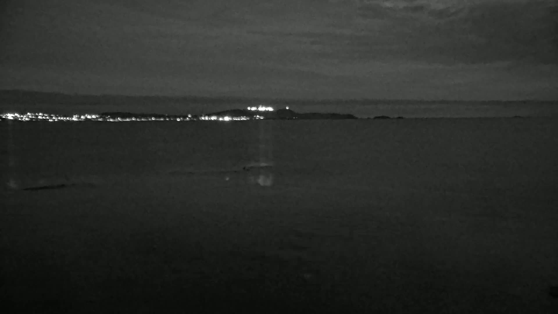A dark, nighttime view of a calm body of water with a distant shoreline illuminated by lights.