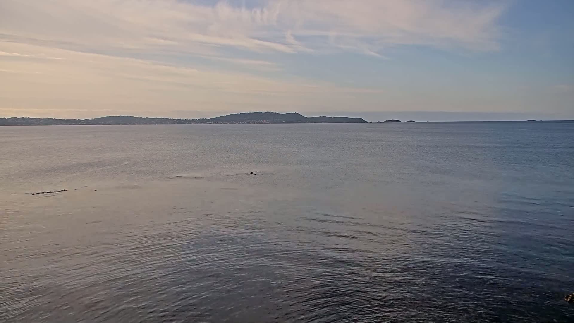 A calm body of water stretches to a distant shoreline with low hills under a partly cloudy sky.