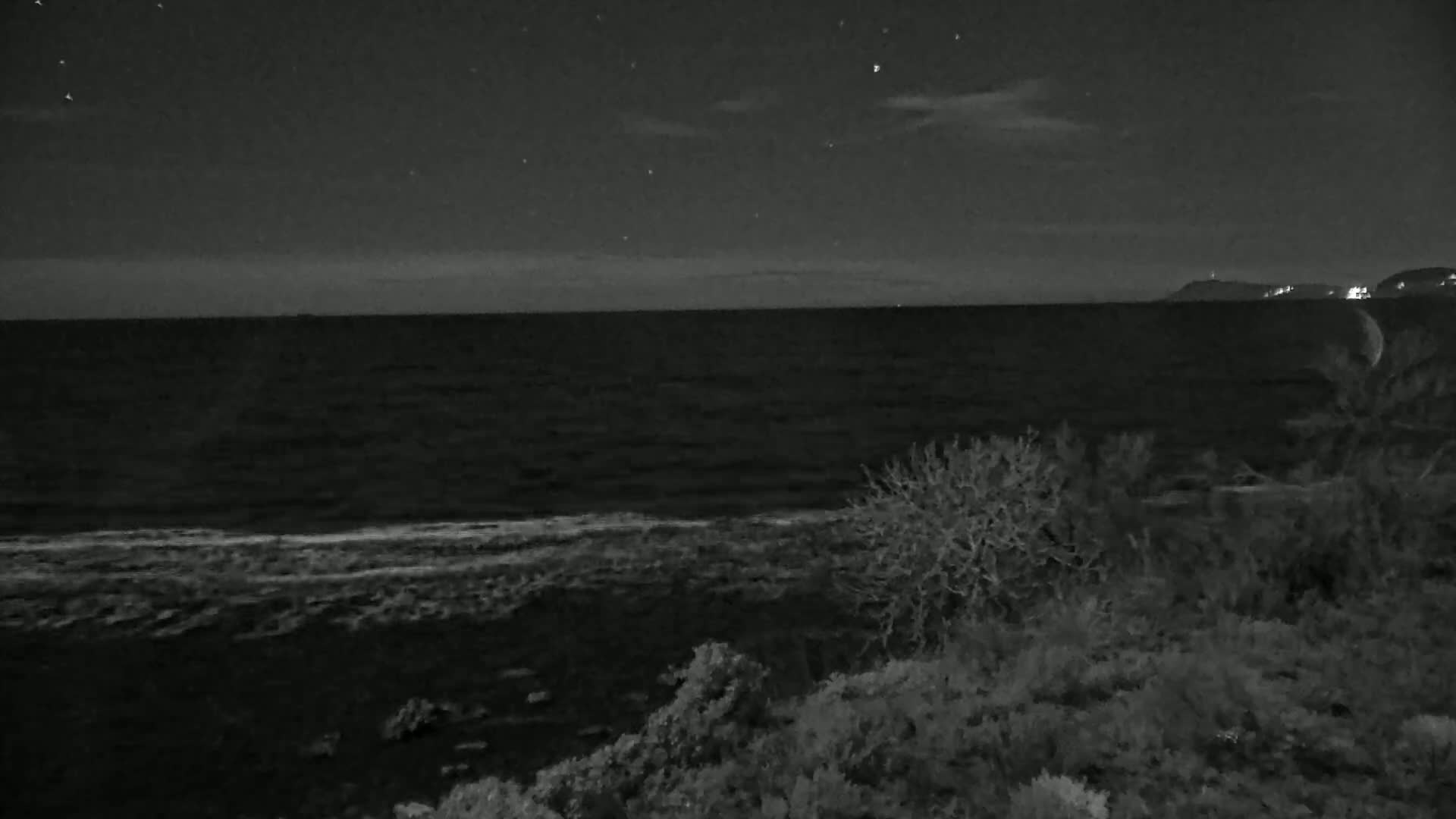 A crescent moon hangs over a dark, wavy ocean under a night sky dotted with stars.