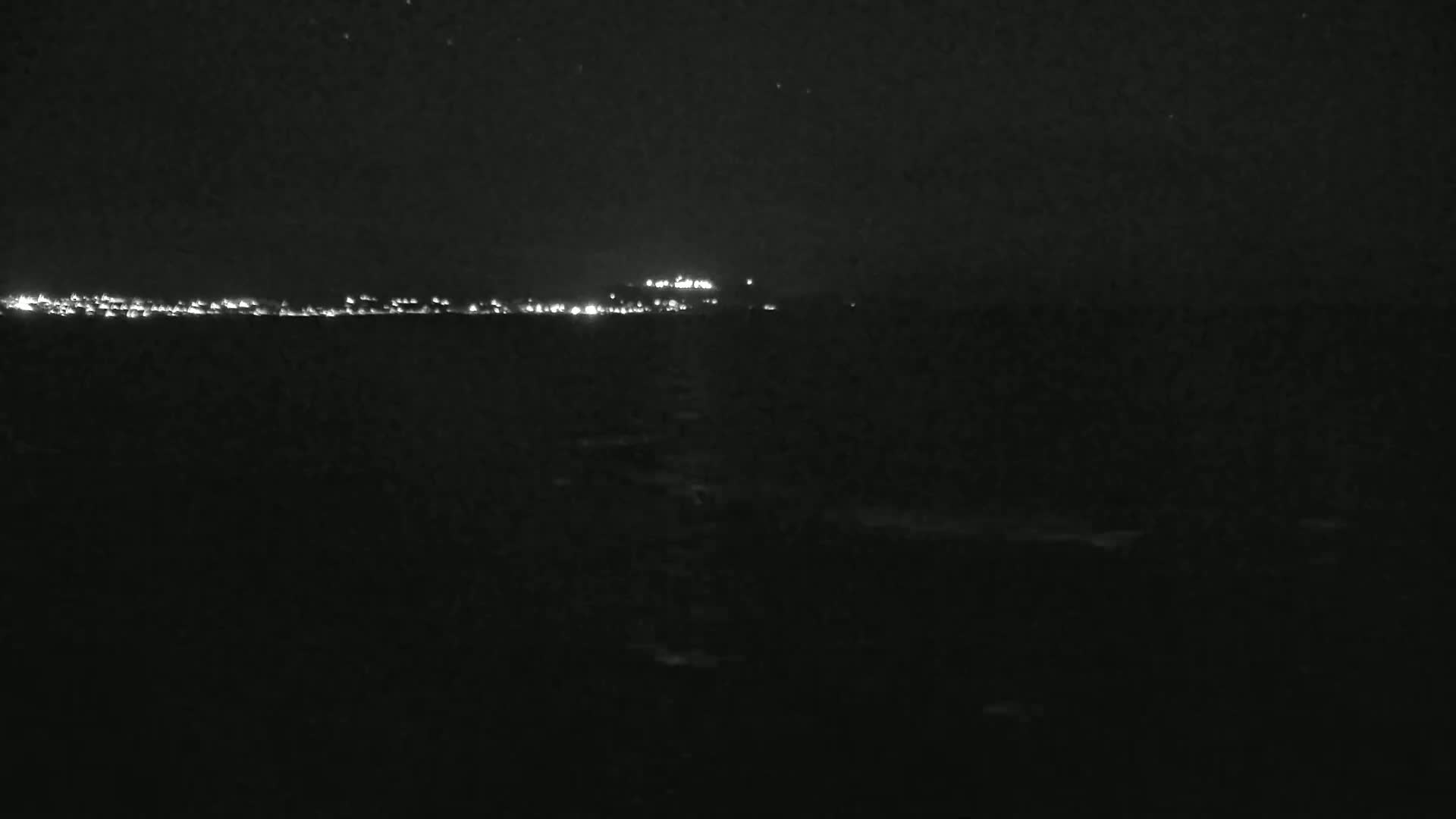 A dark, nighttime view of a distant city skyline illuminated by lights across a body of water under a clear, starry sky.