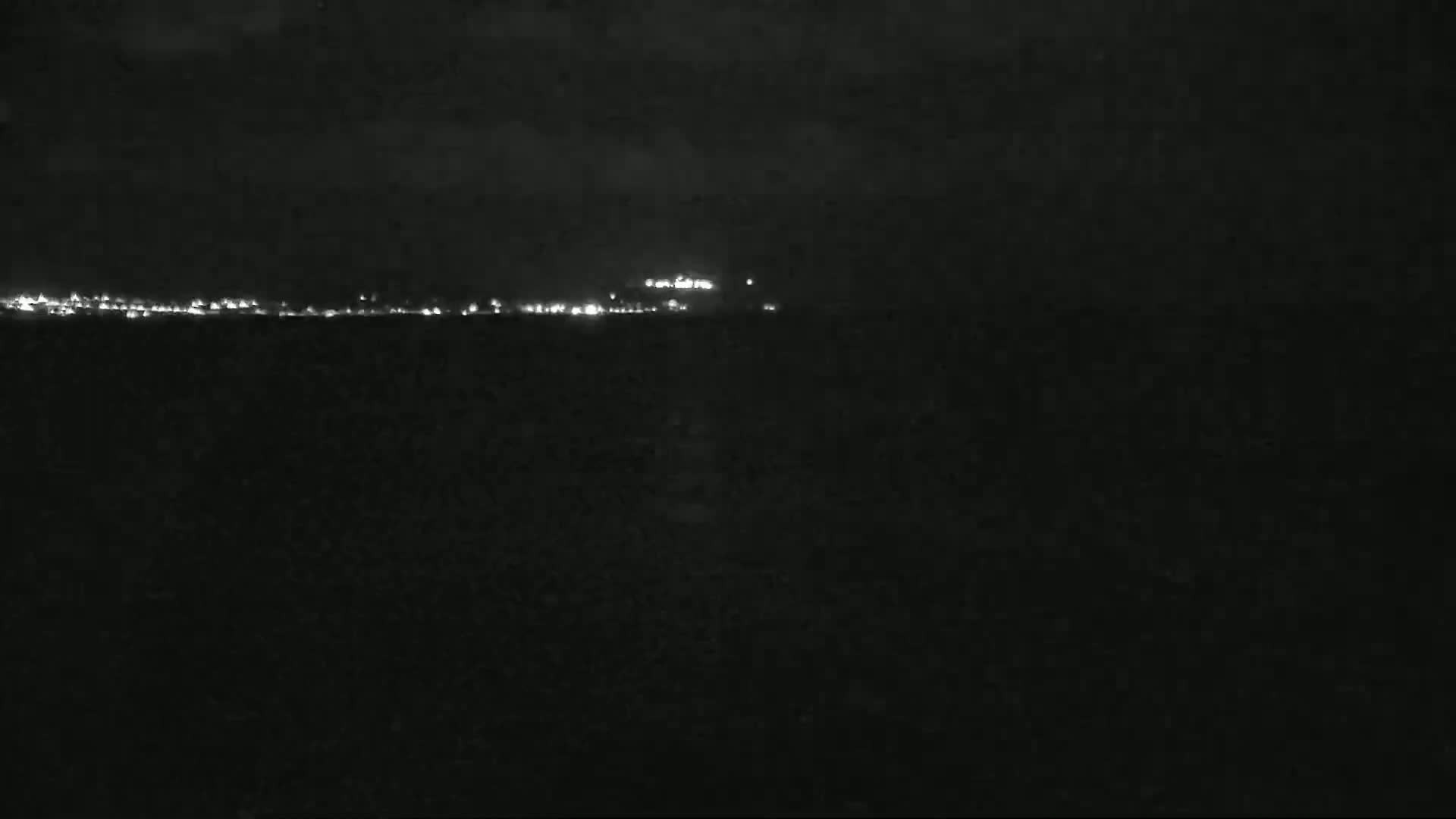 A nighttime view of a distant city skyline illuminated by lights under a dark, cloudy sky.
