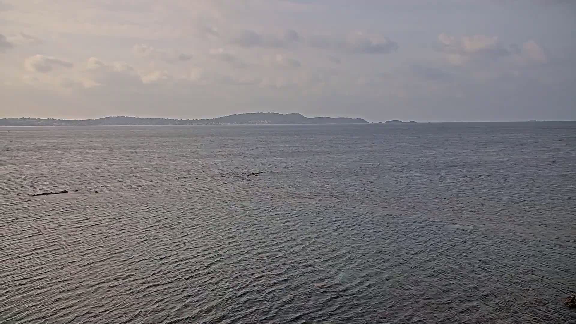 A calm sea with a distant, low-lying landmass under a cloudy sky.