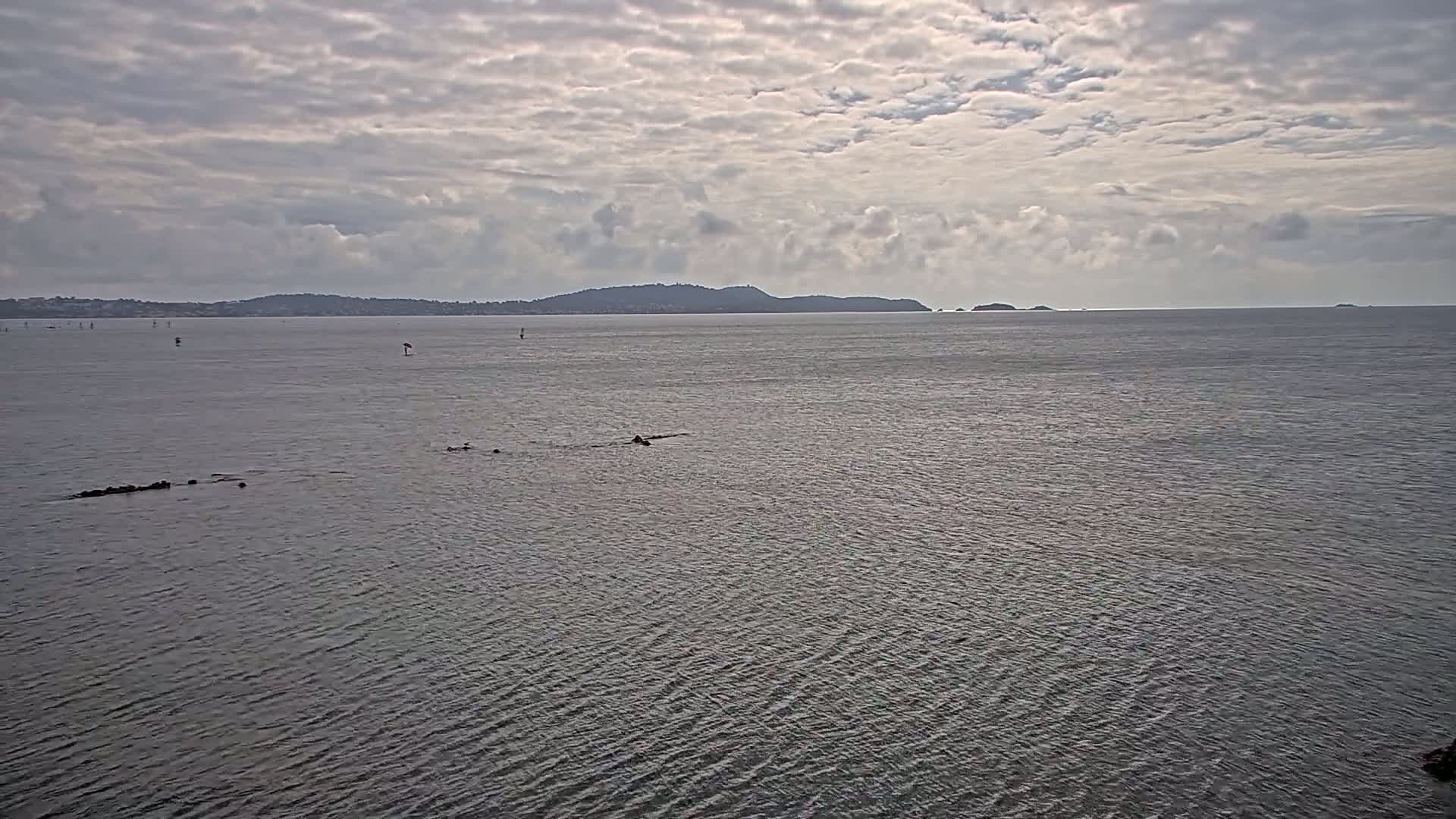 A calm body of water stretches to a distant shoreline under a cloudy sky.