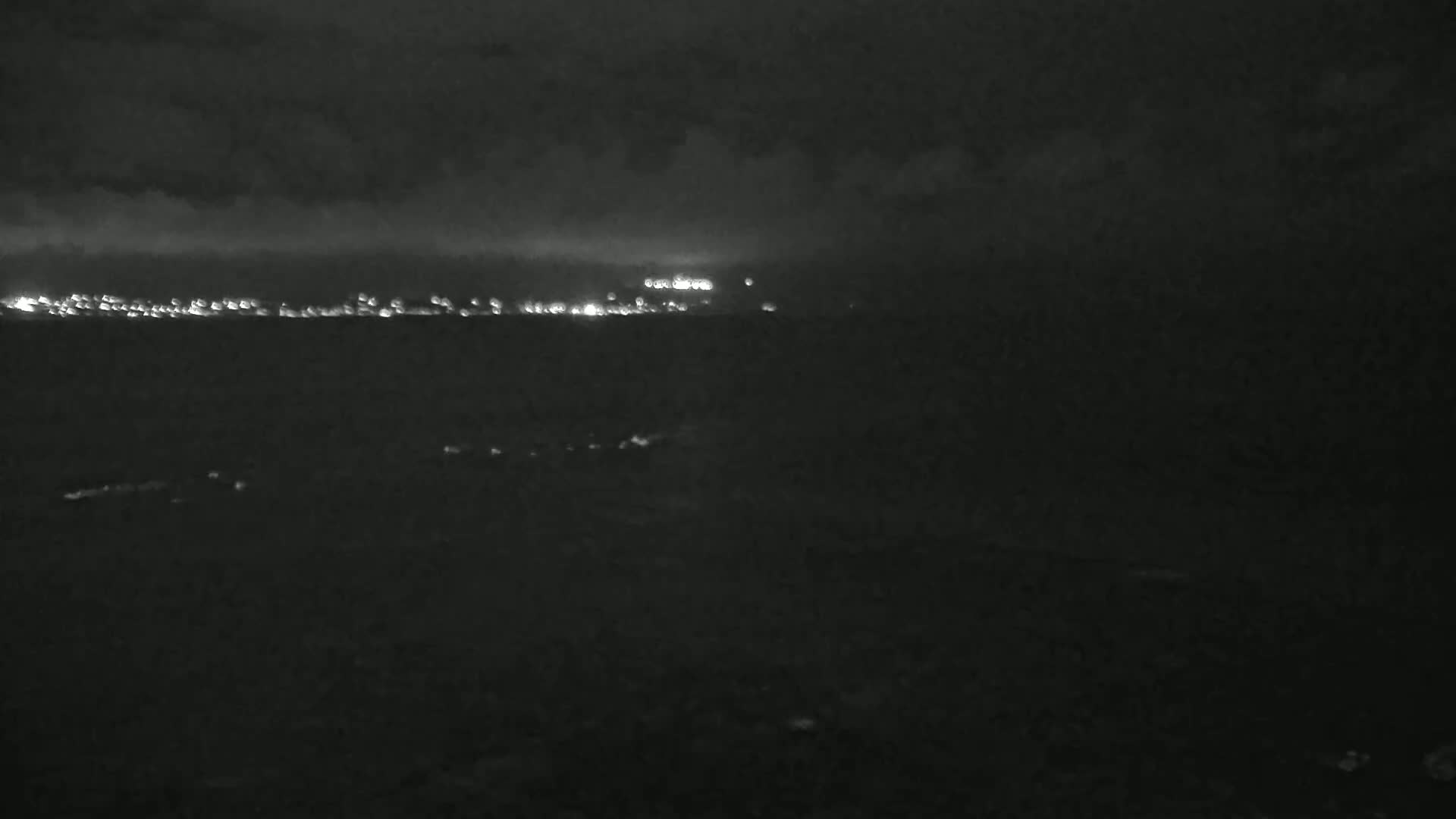 A dark, nighttime scene shows a distant city skyline faintly illuminated by lights under a cloudy sky.