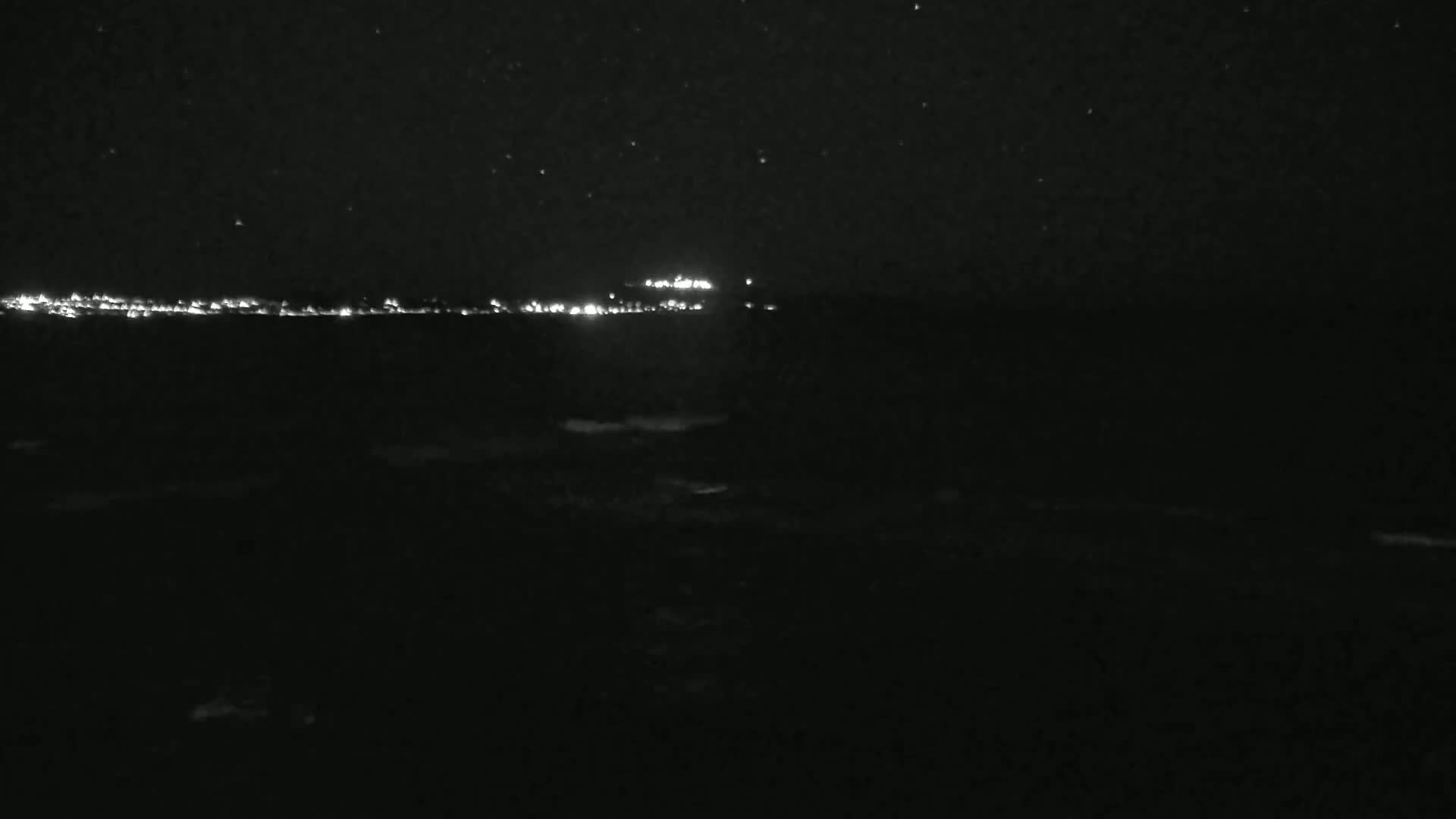 A nighttime view of a distant, dimly lit shoreline under a starry sky.