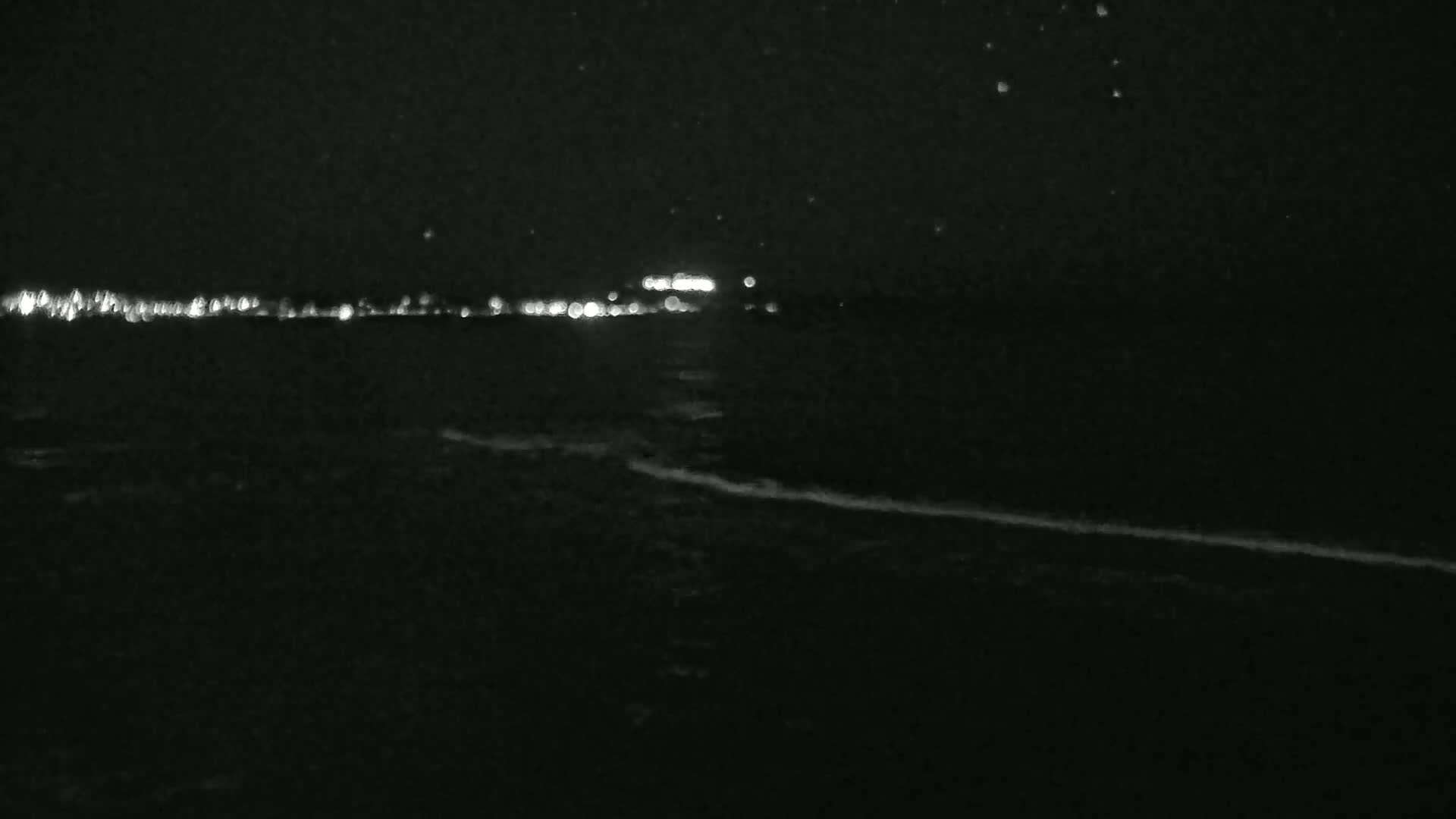 A nighttime view of a dark body of water with a distant line of lights and gently lapping waves.