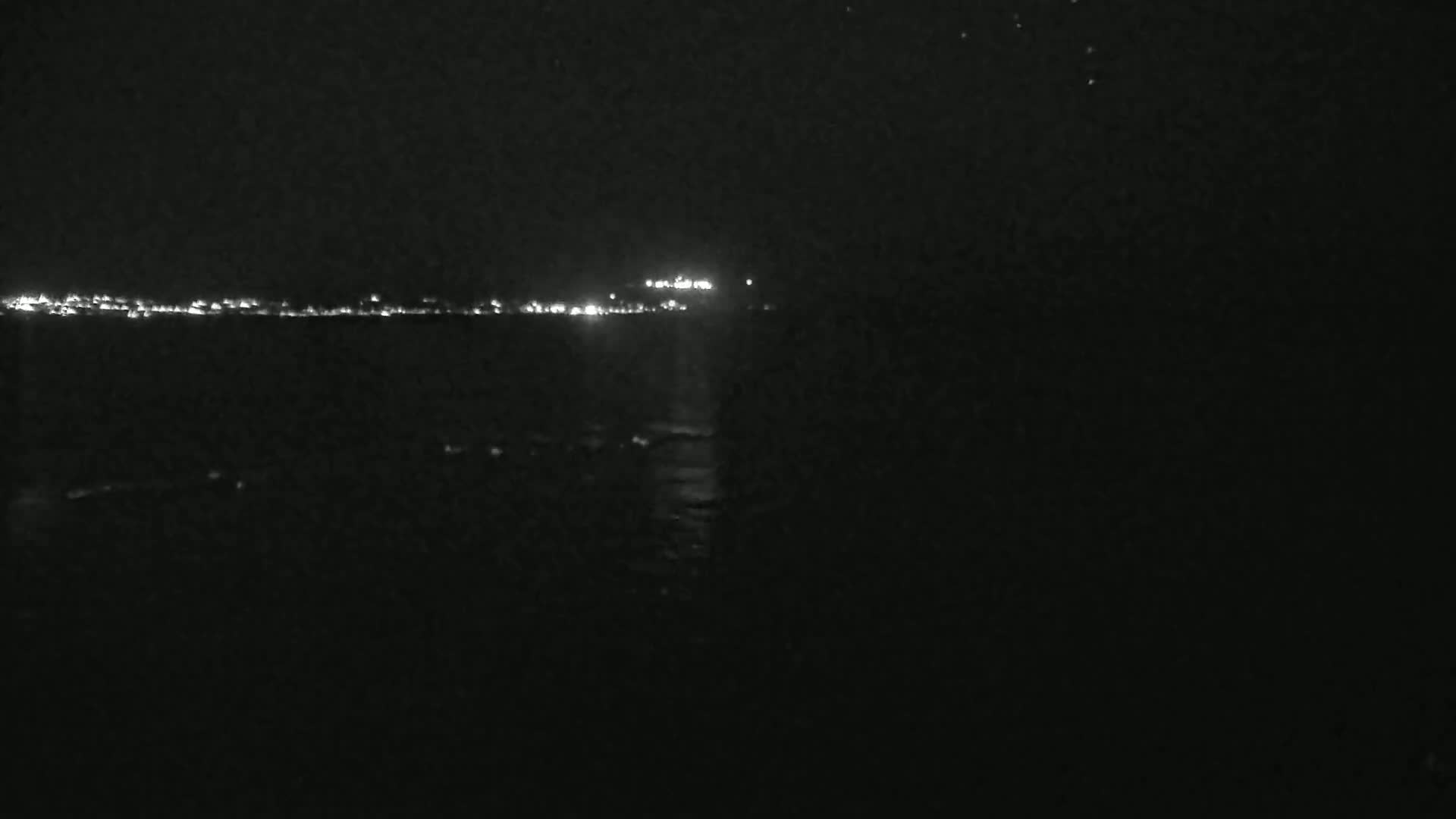 A dark, nighttime view shows a distant shoreline of lights across a body of dark water.