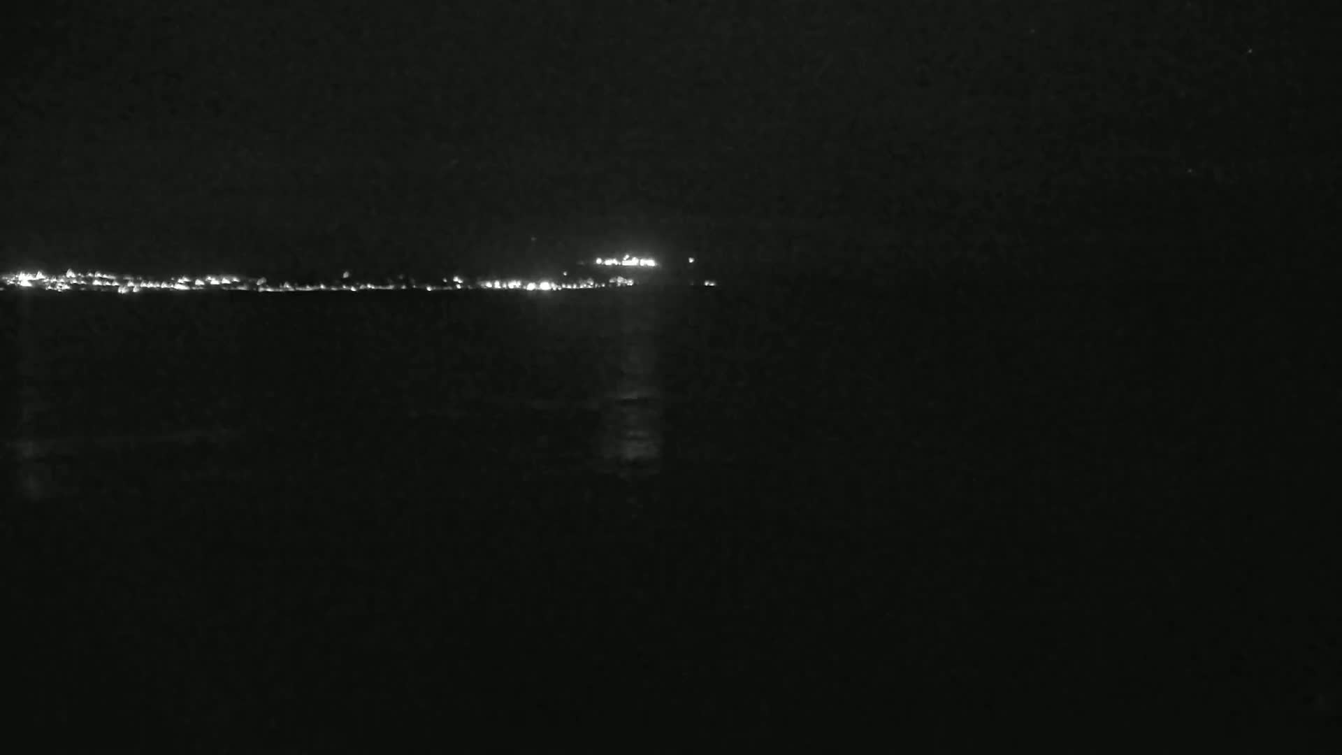 A dark, nighttime scene shows a distant shoreline of lights across a body of water.