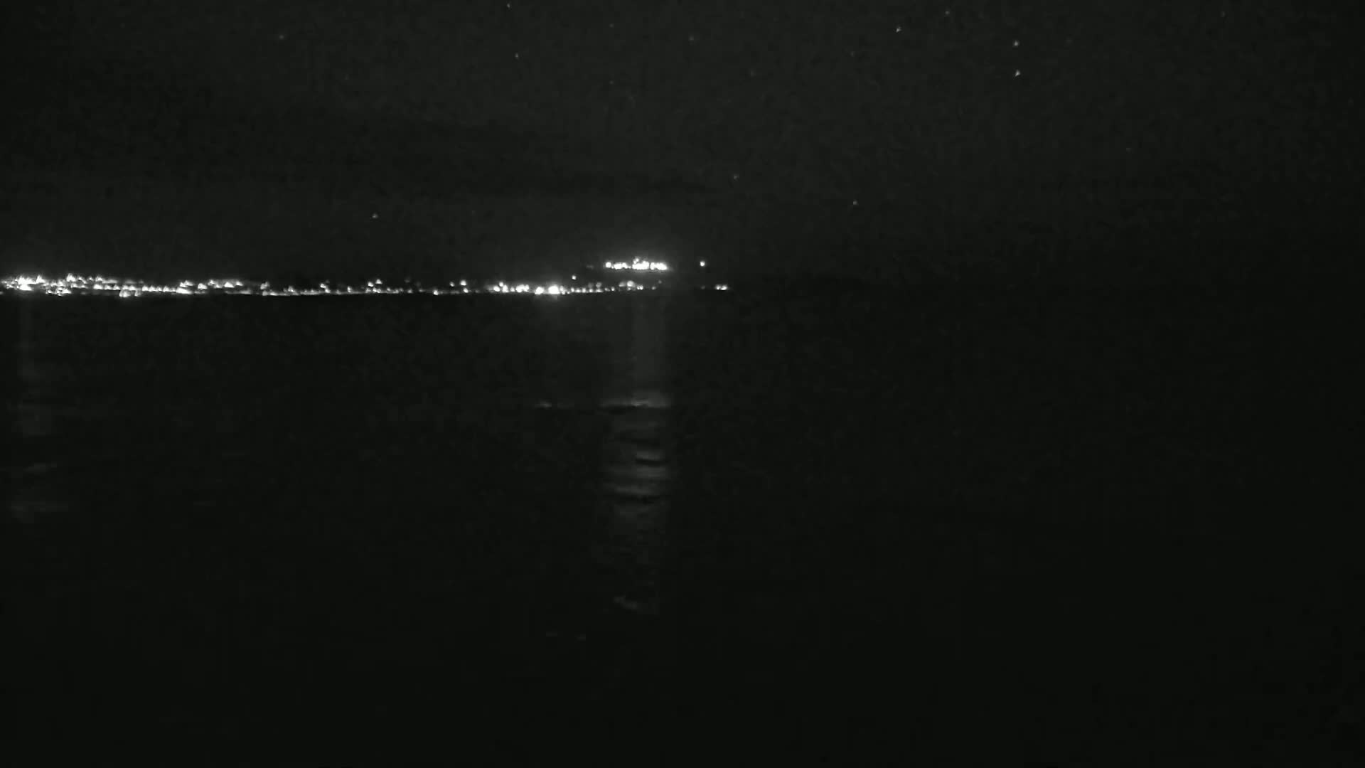 A dark, nighttime view of a calm body of water with a distant city skyline faintly illuminated.
