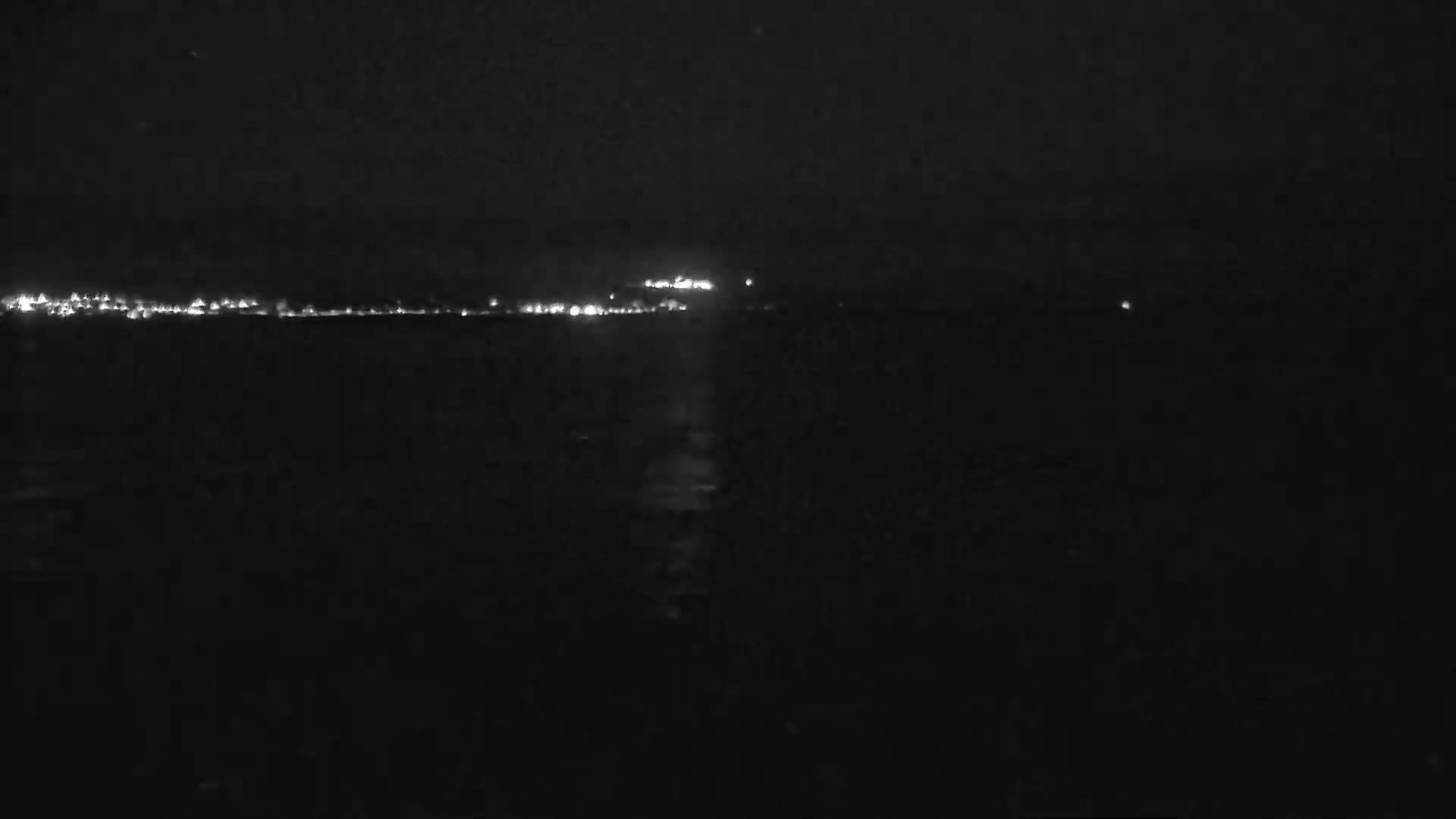 A dark, nighttime scene shows a distant line of lights across a body of water.