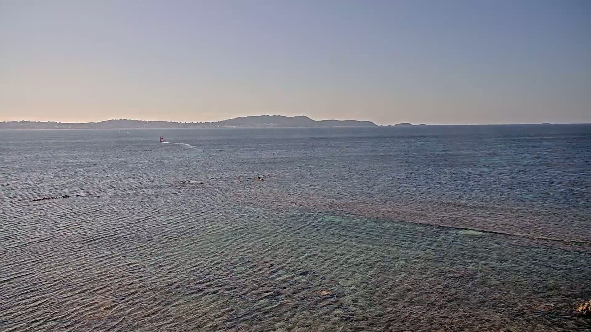 A calm, clear ocean with a distant landmass under a pale sky, and a small vessel visible in the distance.