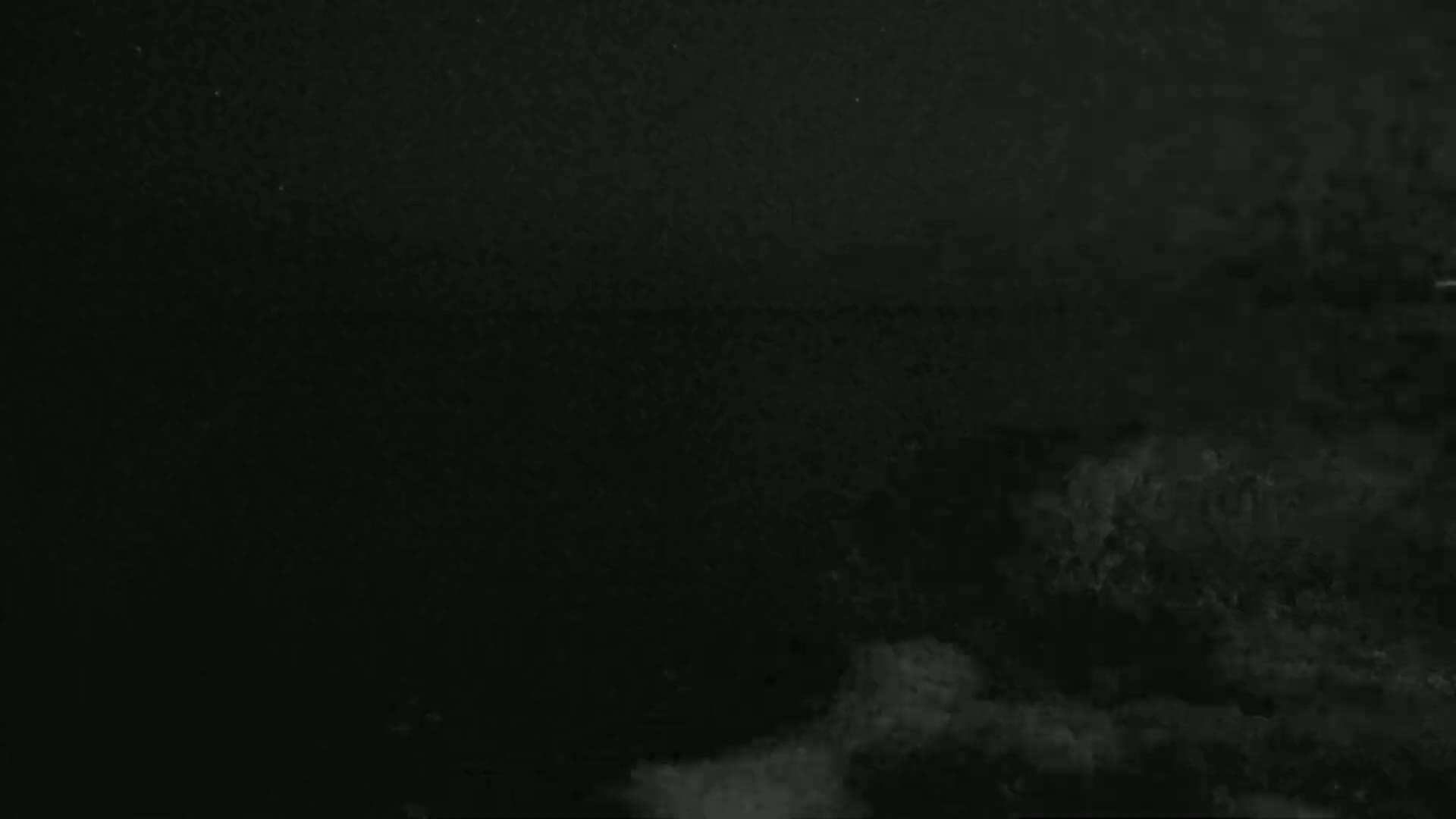 A dark, nighttime image shows a mostly obscured landscape with some lighter areas possibly indicating clouds or fog.