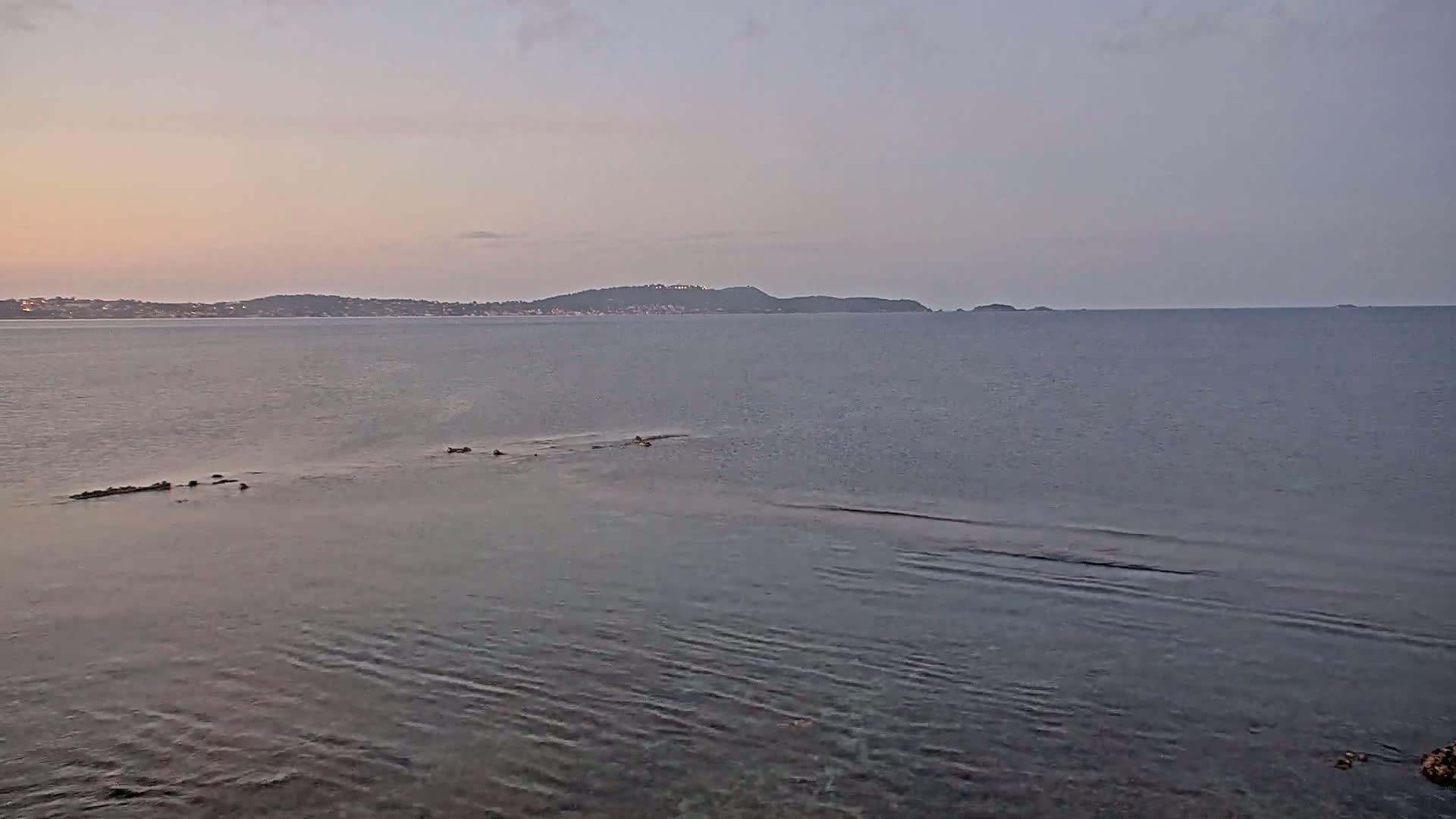A calm, pale-blue sea stretches to a distant shoreline under a soft, overcast sky.