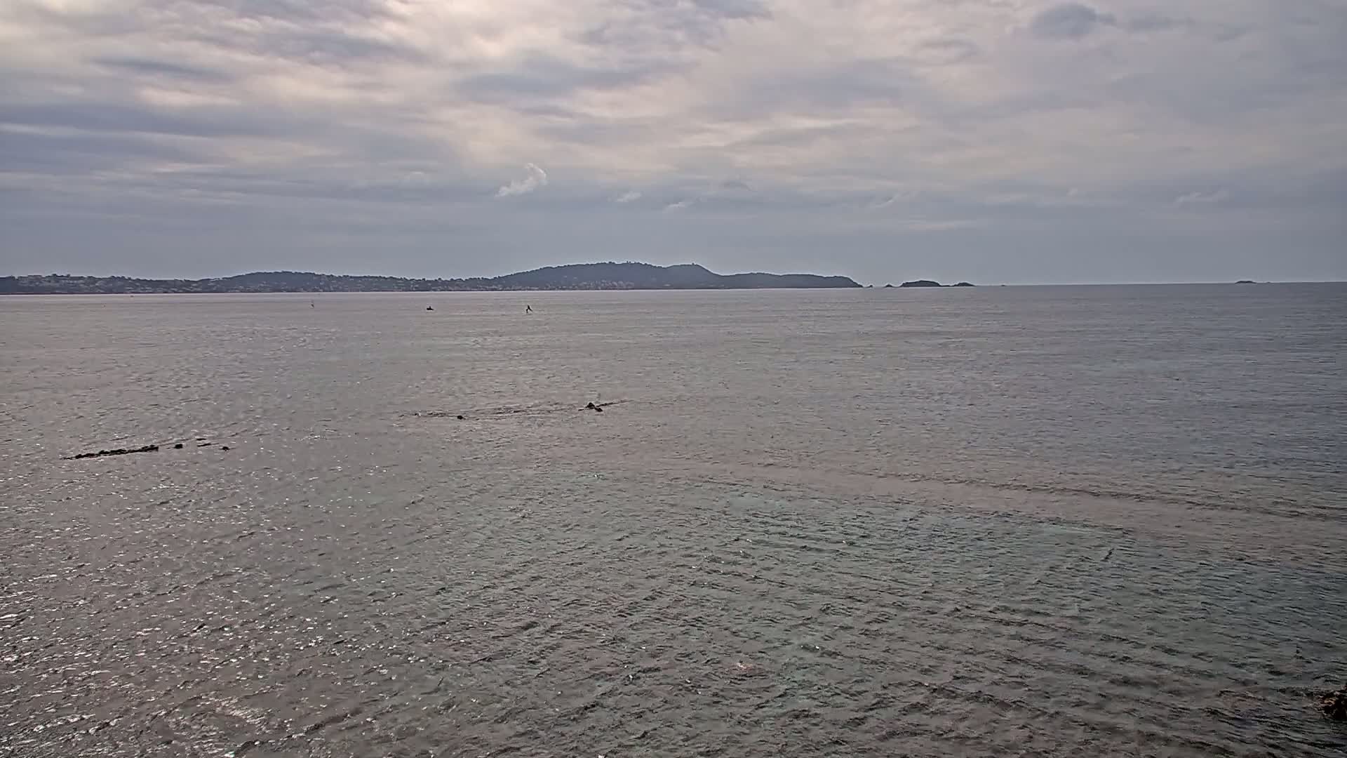 A calm body of water stretches to a distant shoreline under a cloudy sky.