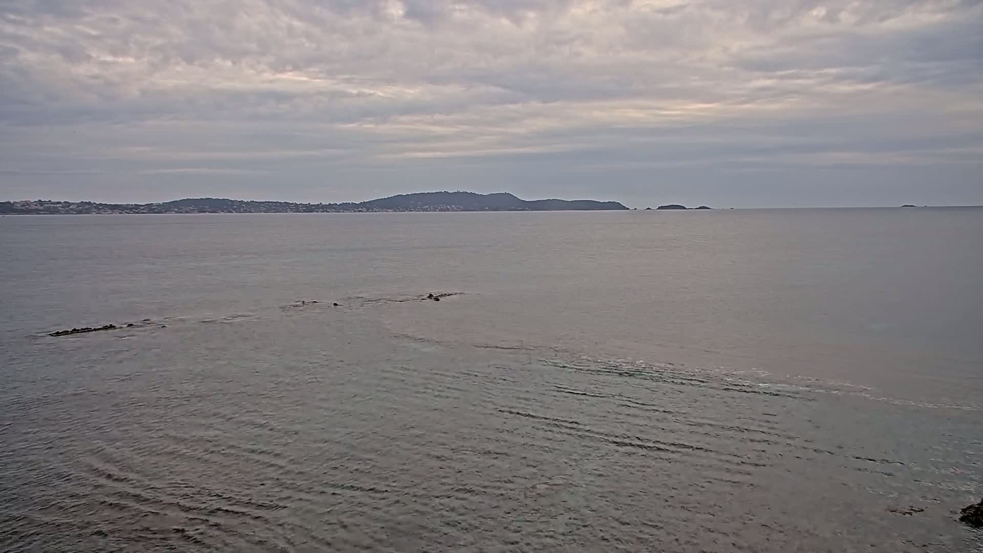 A calm, overcast day reveals a body of water with a distant shoreline featuring hills and small islands.