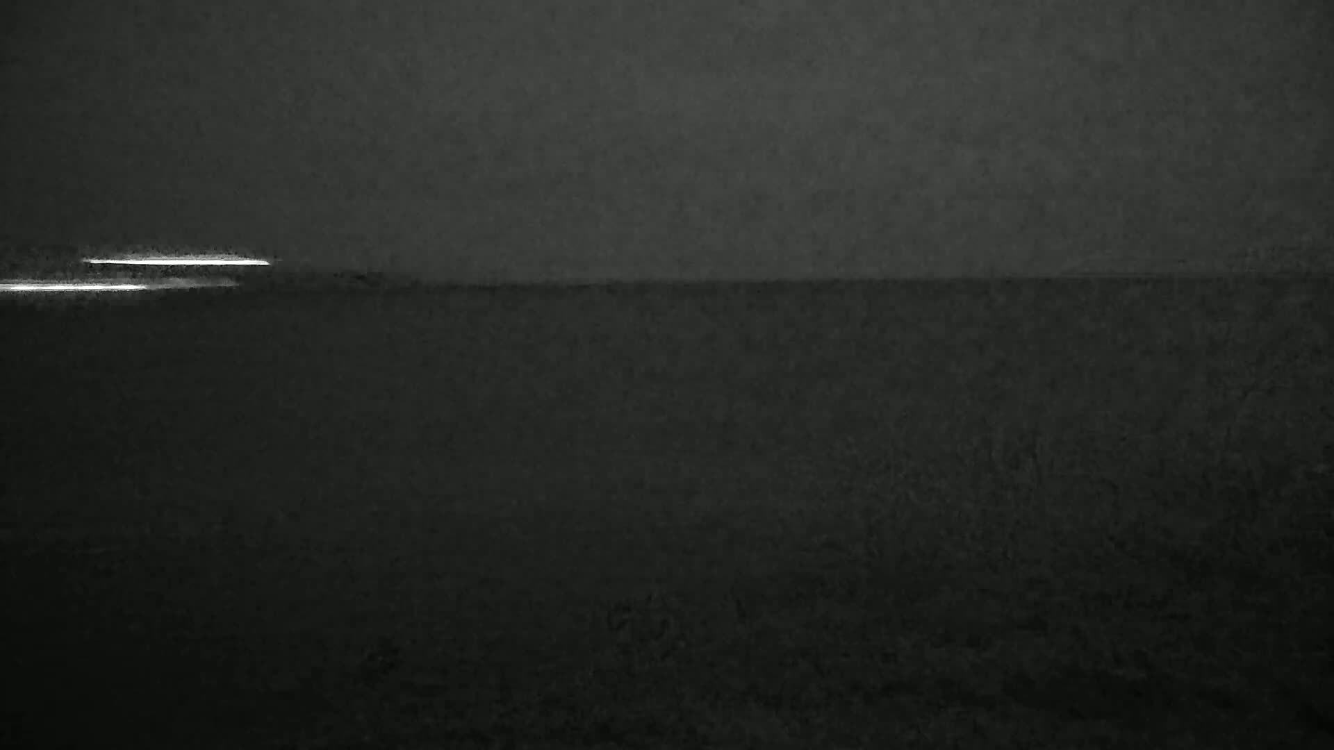 A dark, overcast sky over a dark body of water, with two faint lights visible on the horizon.