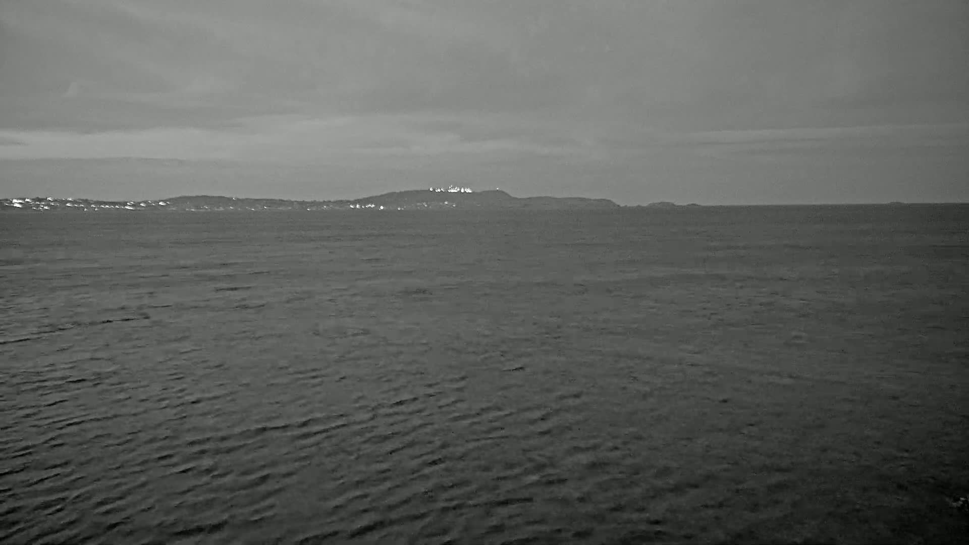 A calm, gray sea stretches to a distant, low-lying landmass under a cloudy sky.