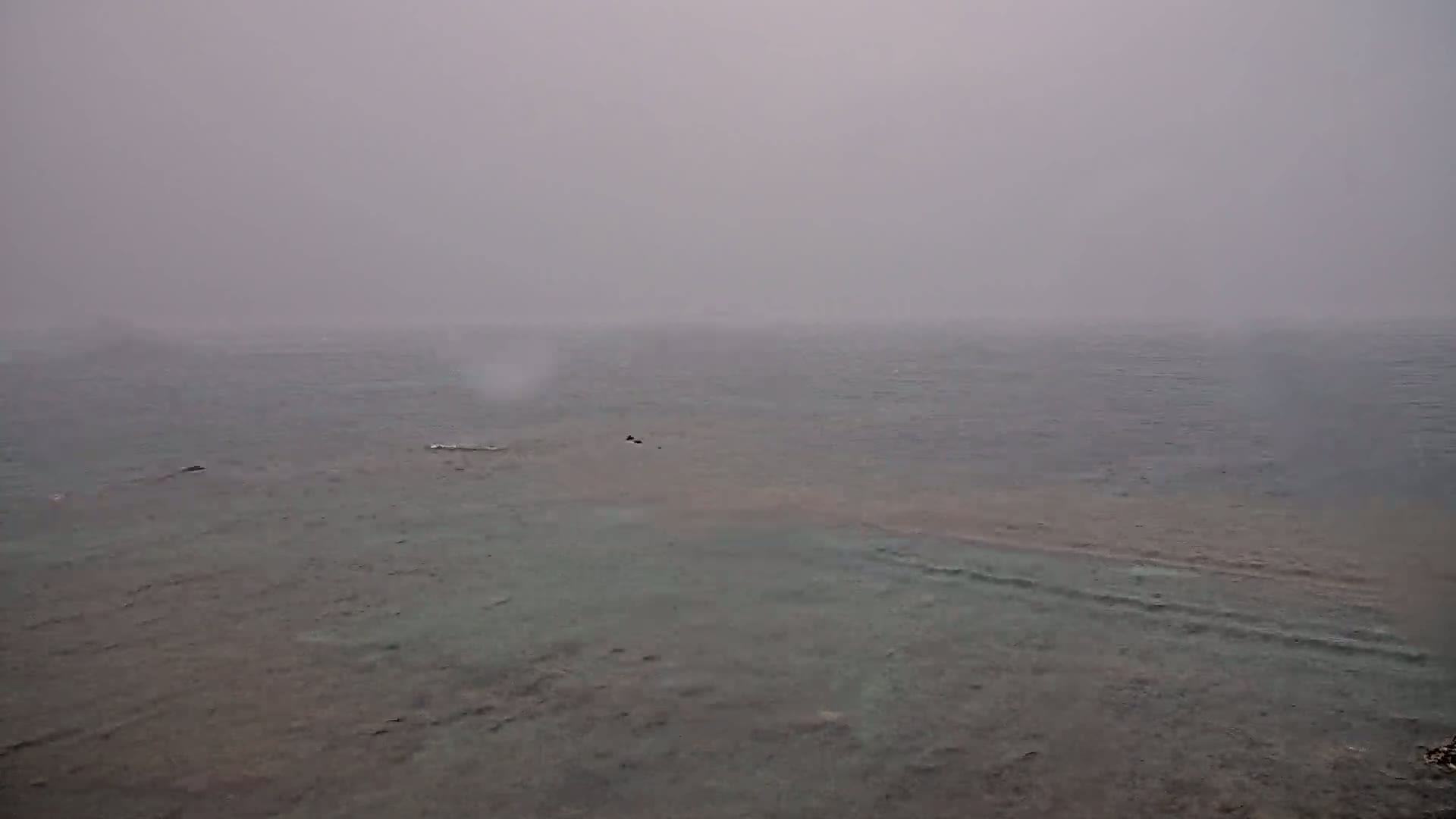 A hazy, overcast day reveals a calm body of water with a partially visible shallow section near the shore.