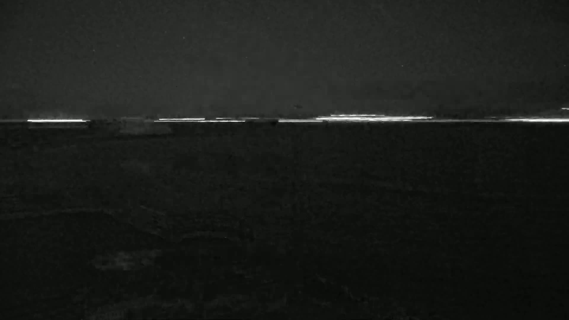A nighttime, low-light image shows a faint, horizontal line of light on the horizon above a dark, textured ground.
