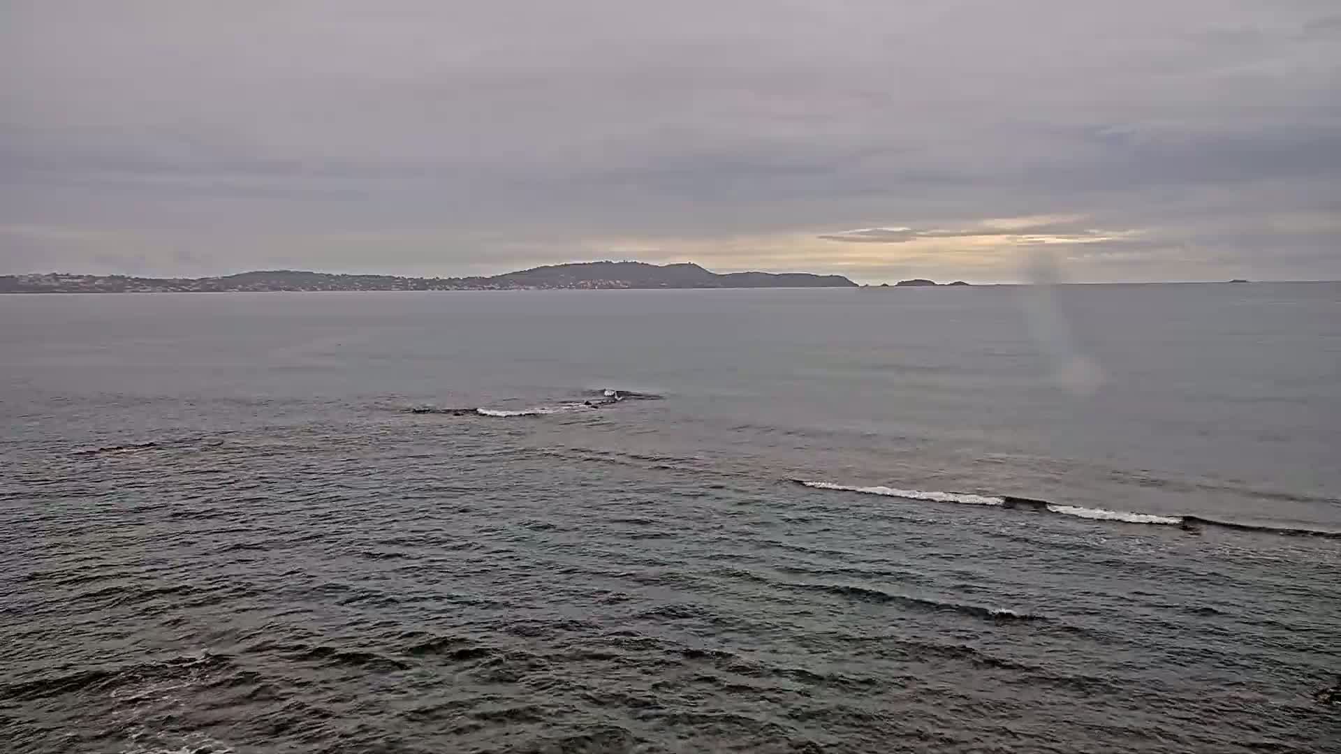 A calm, gray sea stretches to a distant shoreline under an overcast sky.