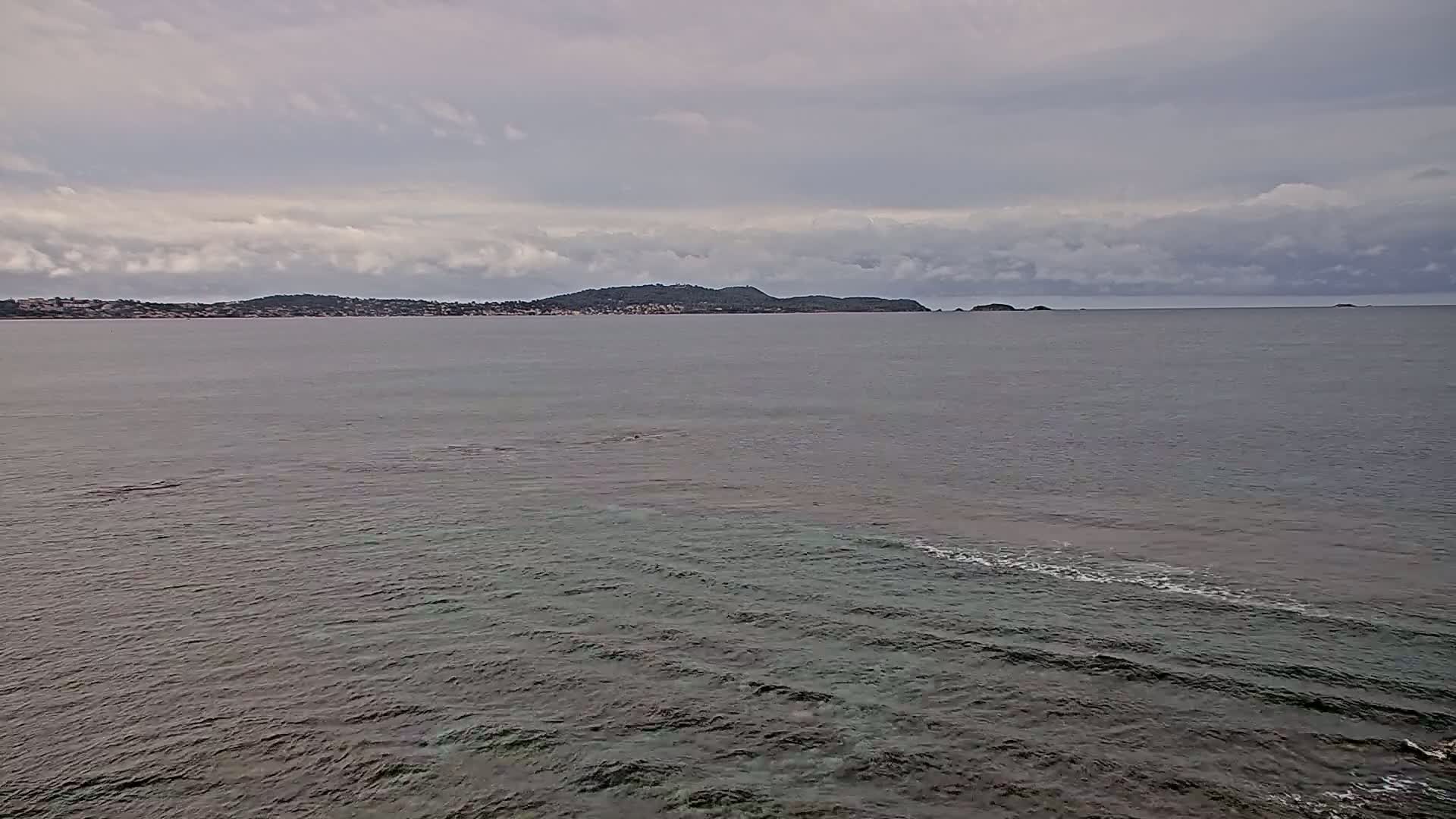 A calm sea with slightly wavy water stretches toward a distant coastline under a cloudy sky.