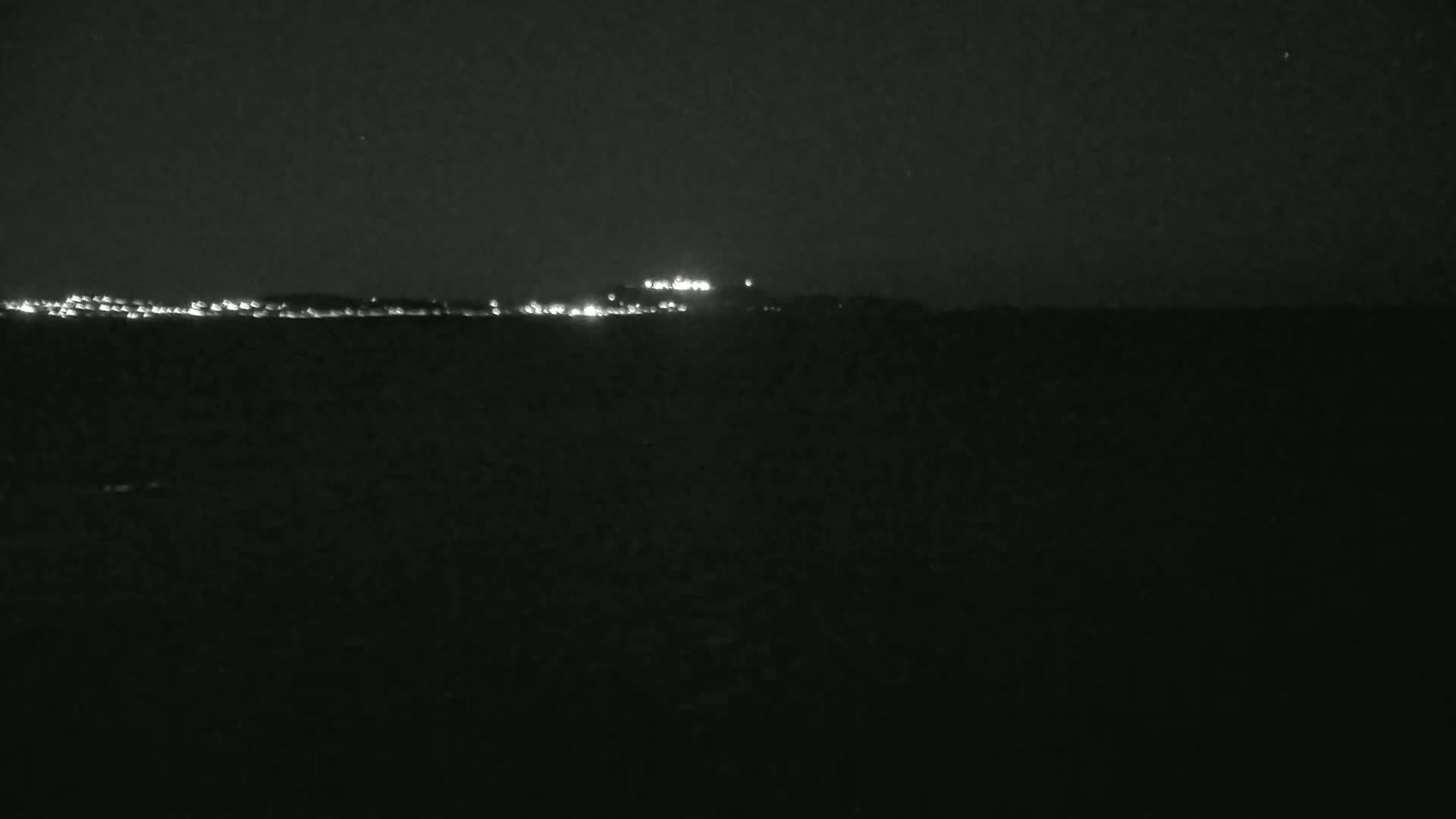 A distant line of lights illuminates a dark, nighttime landscape.