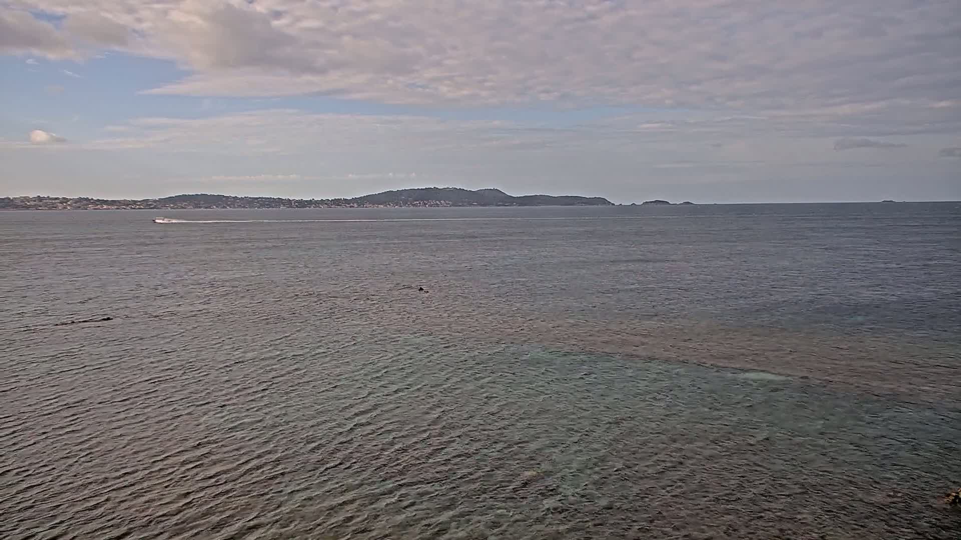 A body of water with a distant landmass under a partly cloudy sky shows a boat in the middle ground.