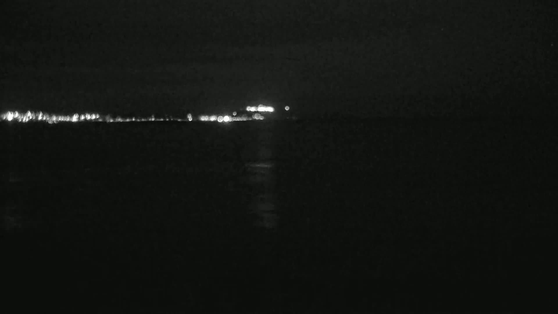 A dark body of water reflects the distant lights of a city at night.