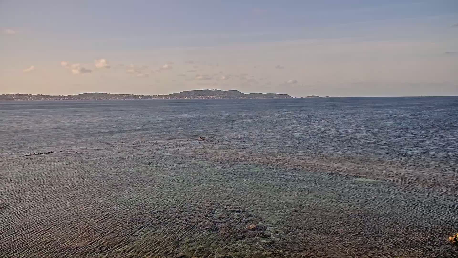 A calm, clear ocean stretches to a distant shoreline under a pale sky with a few clouds.