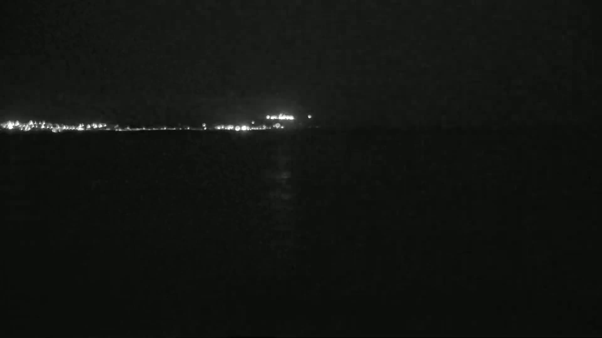 A nighttime view shows a distant line of lights across a dark body of water.