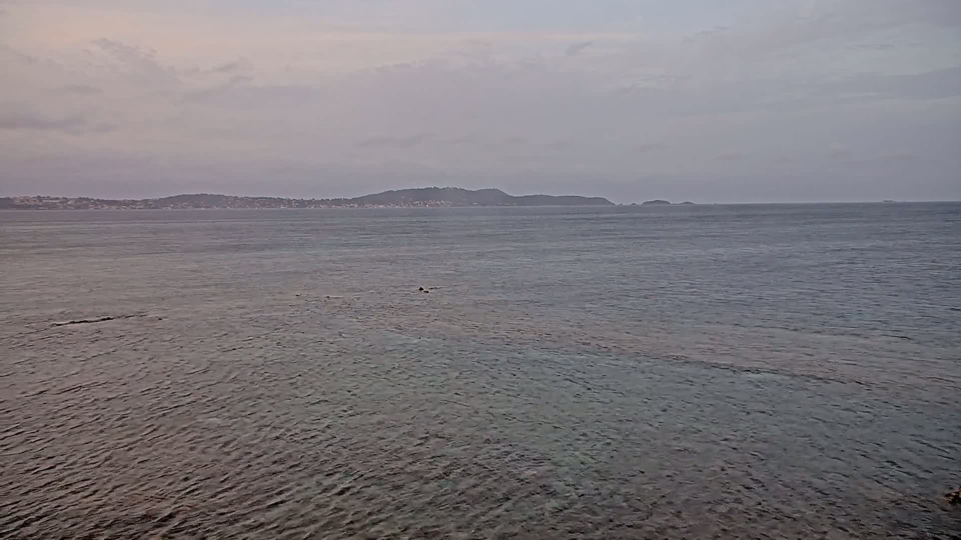 A calm, overcast day shows a body of water with a distant shoreline of low hills and a few small islands.
