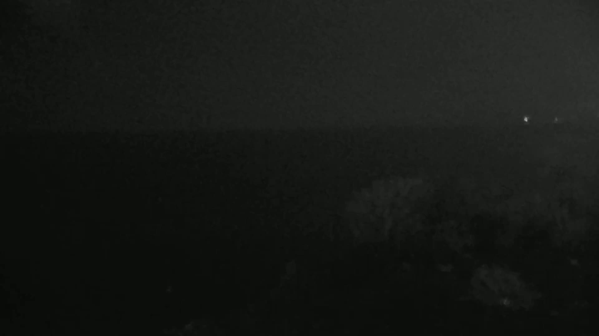 A dark, hazy nighttime scene shows a blurry, indistinct landscape with a few faint lights in the distance.