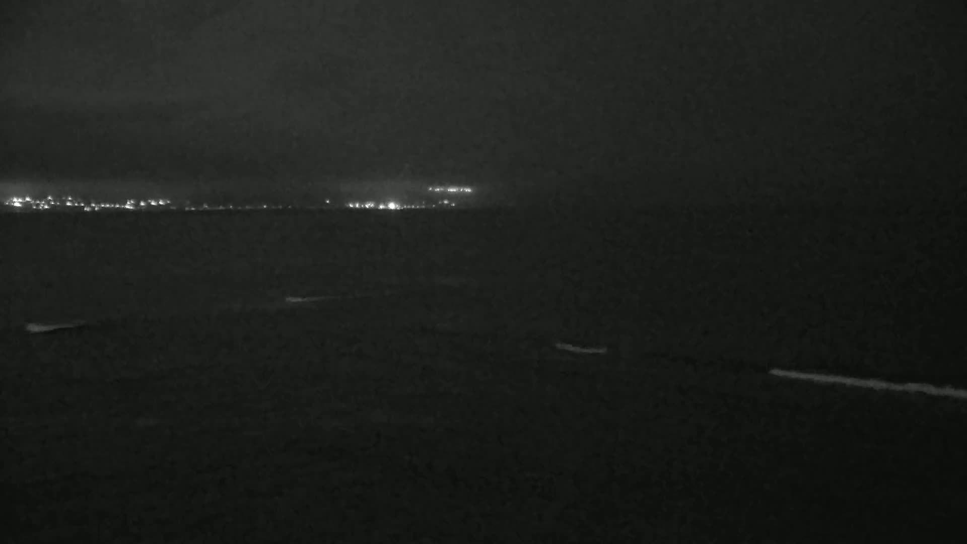 A dark, nighttime view of a body of water with a distant city skyline faintly visible under an overcast sky.
