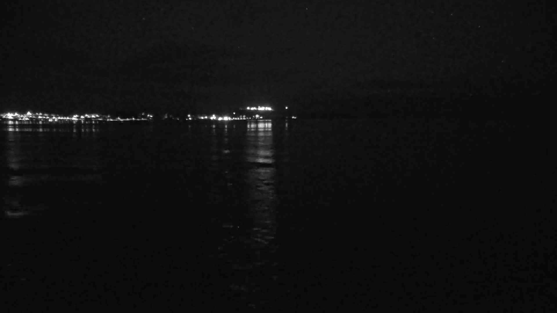 A dark body of water reflects the lights of a distant city at night under a clear, starlit sky.