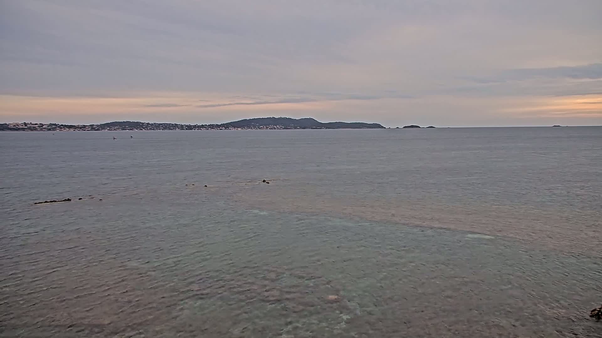 A calm sea with a distant island under a cloudy sky.