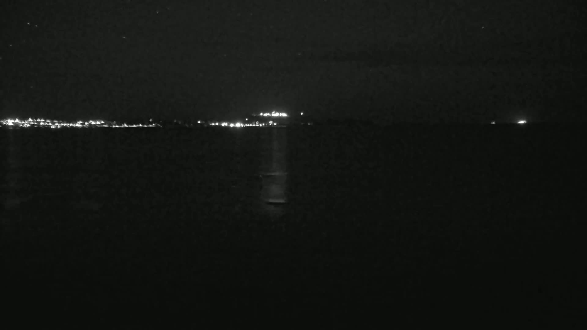 A dark body of water is seen at night, with a distant shoreline faintly illuminated by lights.