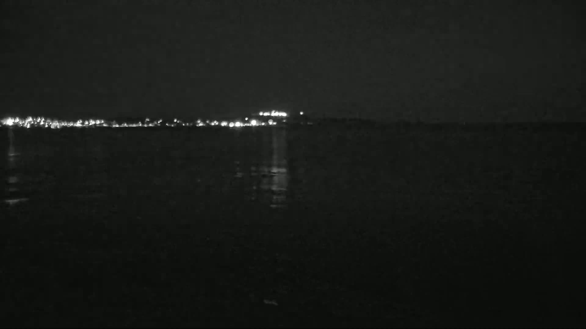 A dark body of water reflects the lights of a distant town at night.