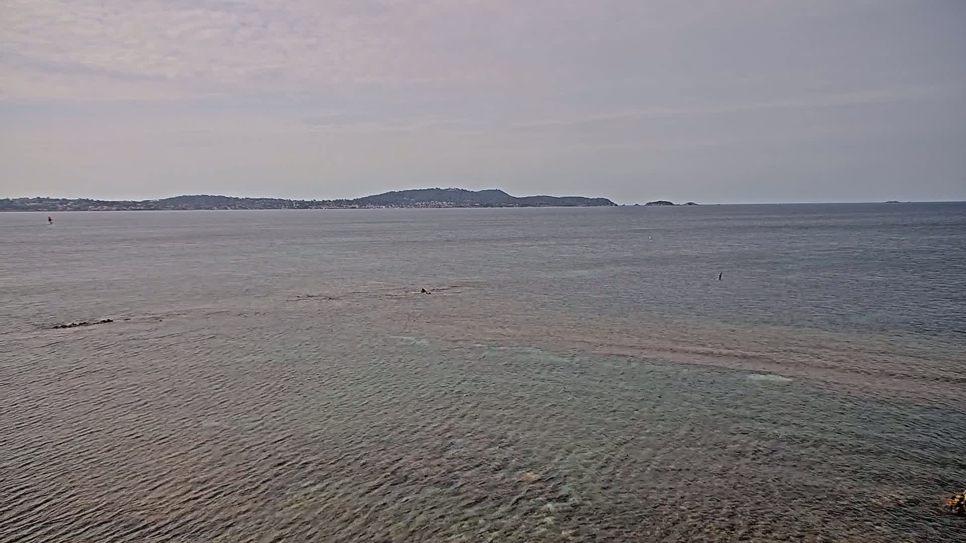 A calm, overcast day shows a view of a body of water with a distant island and shallows visible in the foreground.