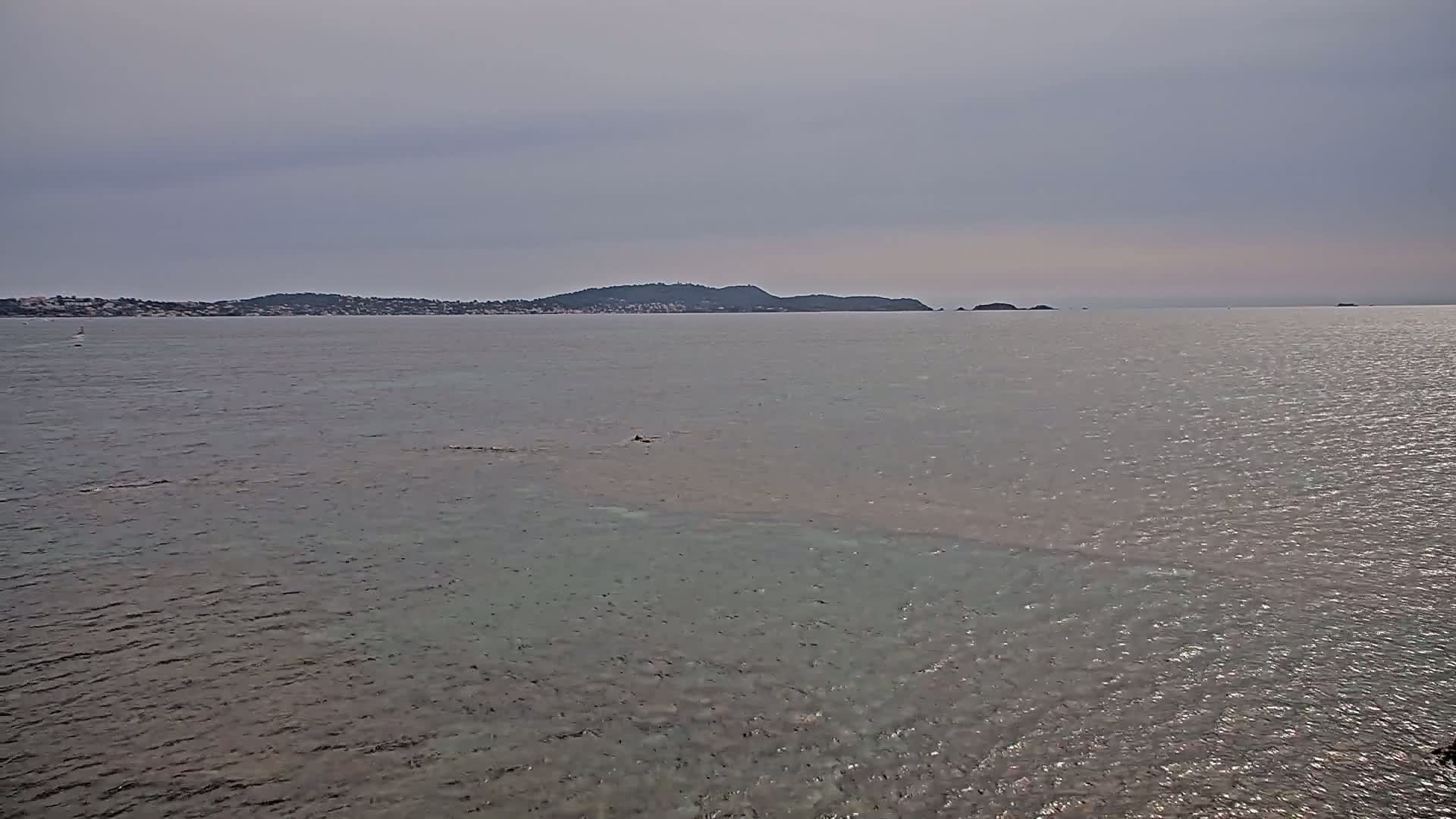 A calm, gray-sky day reveals a body of water with a distant shoreline featuring a low-lying hill and small islands.